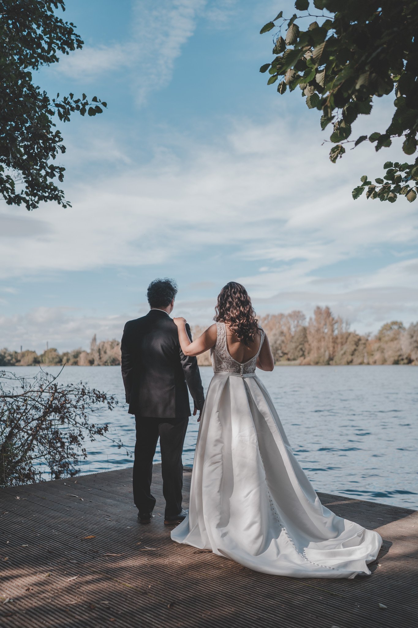 Bride and groom with their backs at the camera, watching over Delapre Lake in Northampton