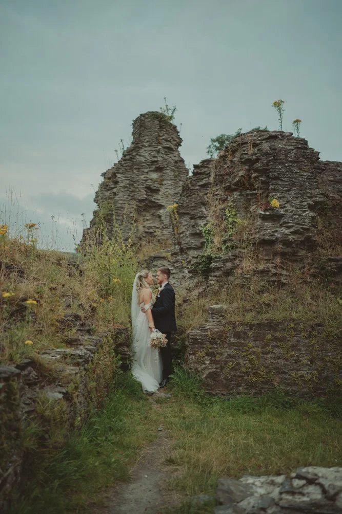 Bride and groom photographed kissing in front of ruins, on their wedding day in Wales
