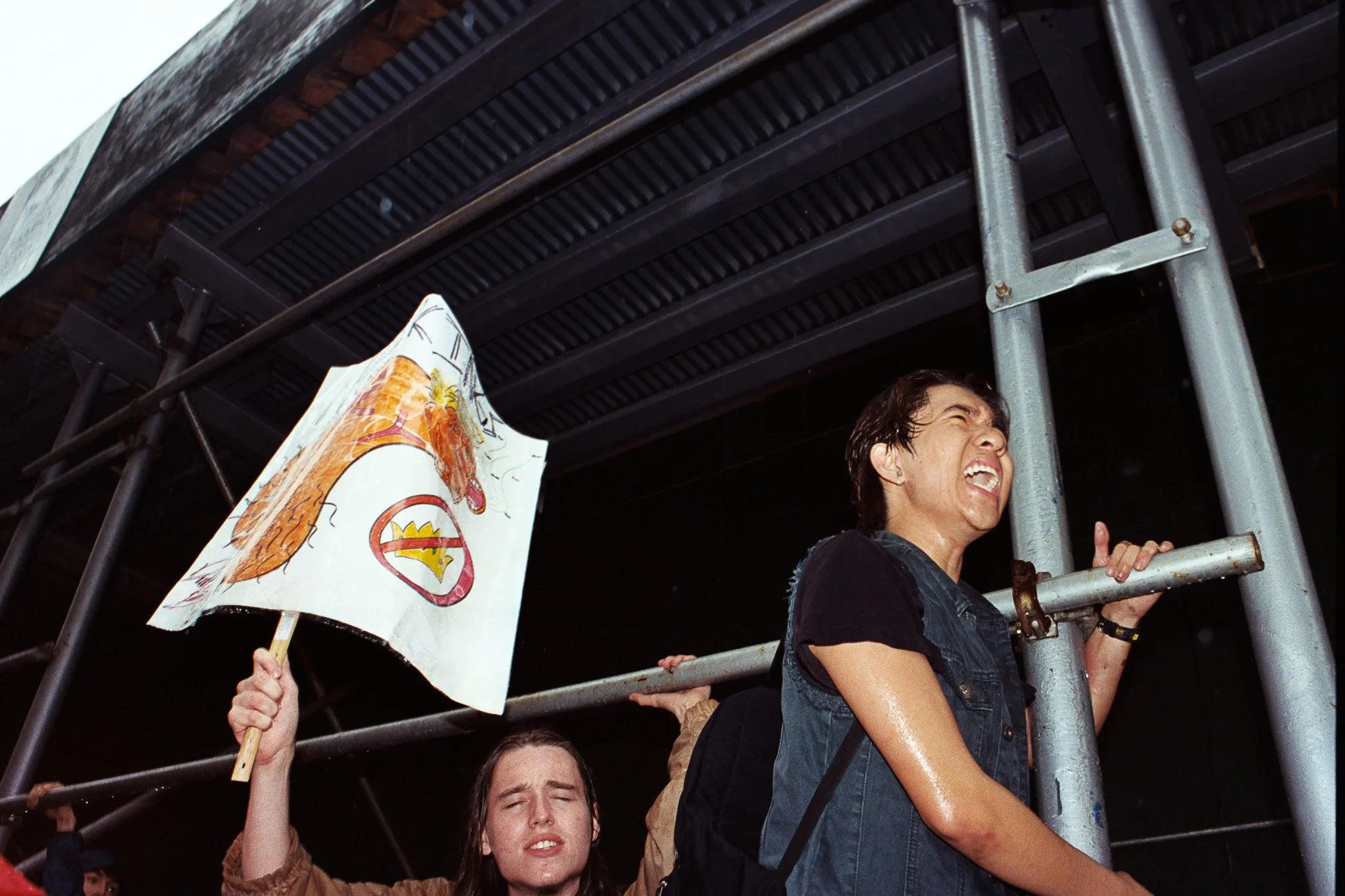 People celebrating on a scaffold with one holding a flag and another with a smile, under a brick and metal overhead structure.