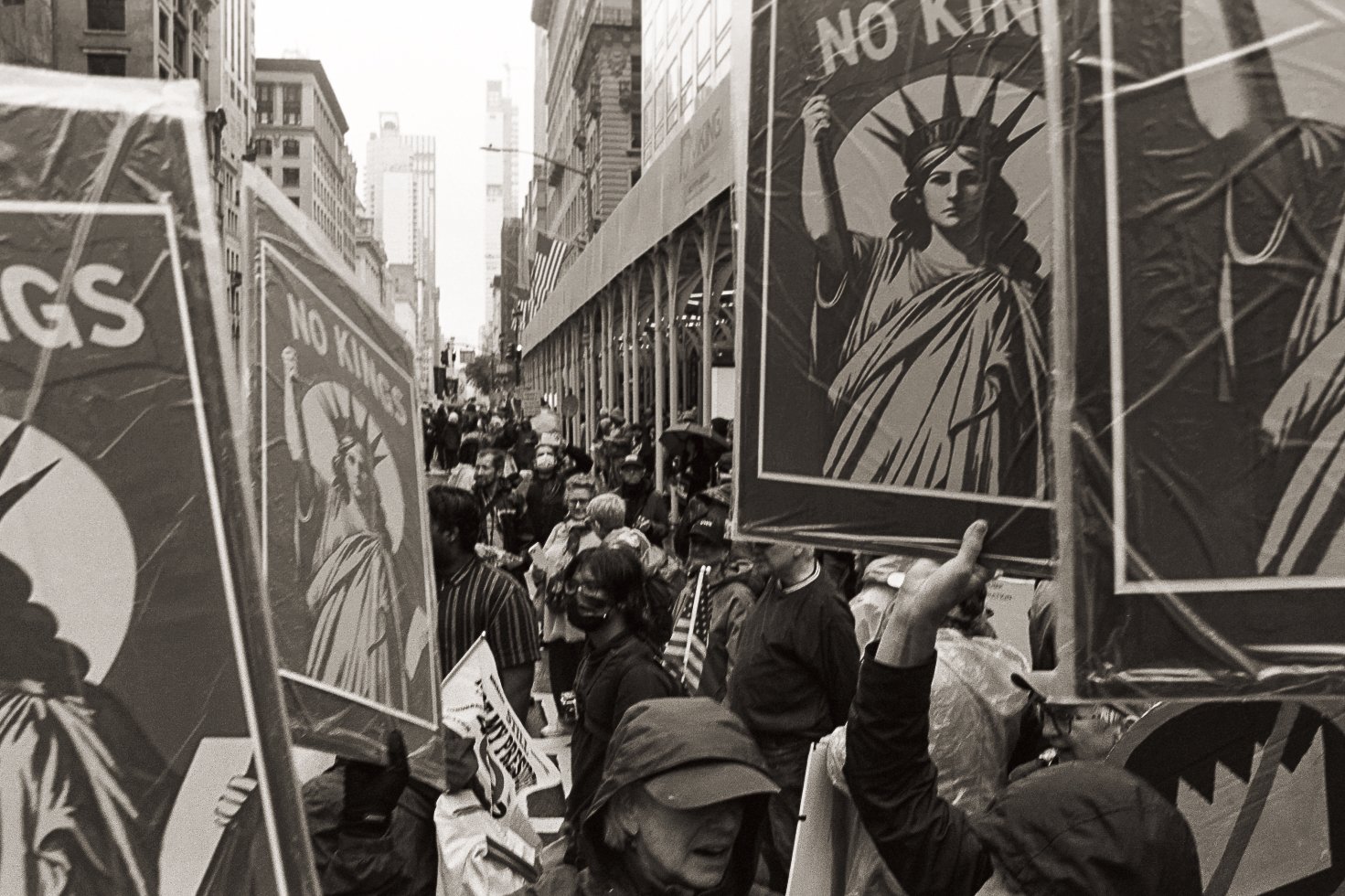 Crowd of protesters holding signs depicting the Statue of Liberty with a "NO KIDS" message during a demonstration on a city street in black and white.