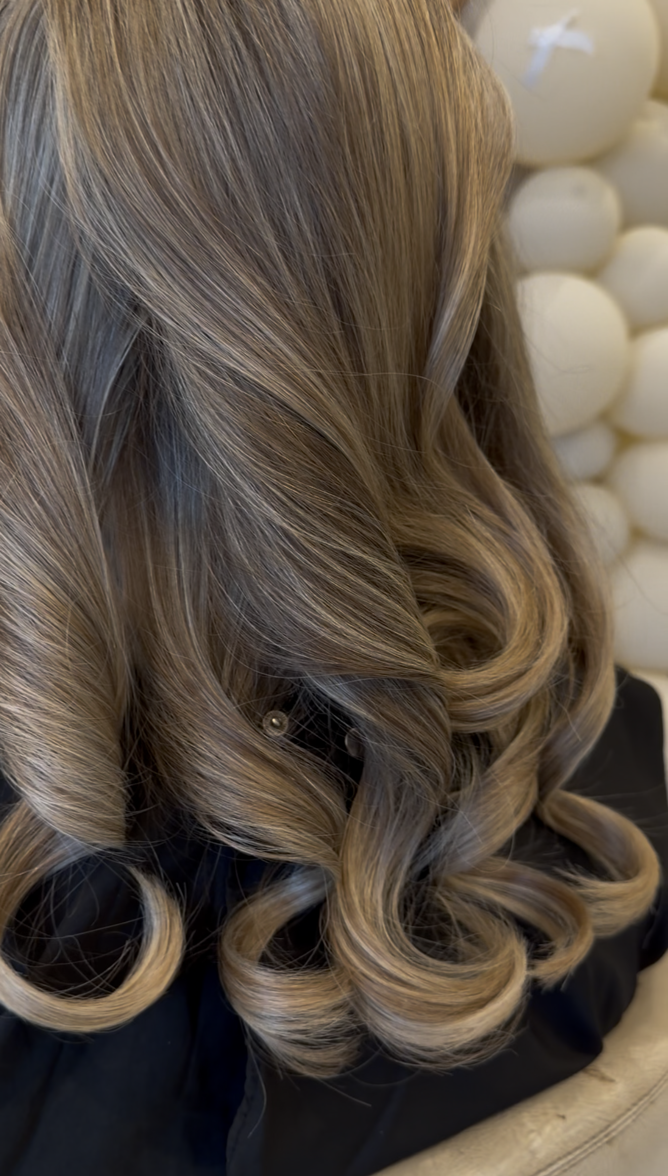 Close-up of long, wavy, blonde hair with highlights, styled in loose curls.