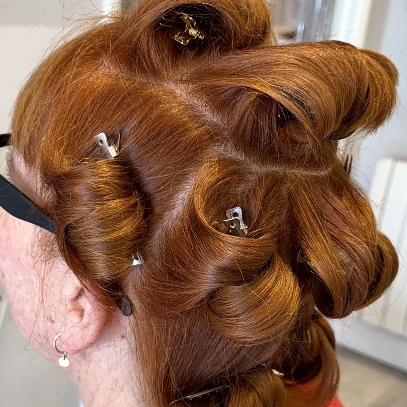 Red hair styled in large curls with hair clips visible, side view of a woman's head.