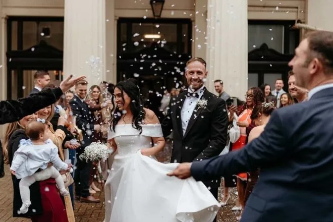 Bride and groom celebrating their wedding as guests throw confetti in the air inside a grand hall.