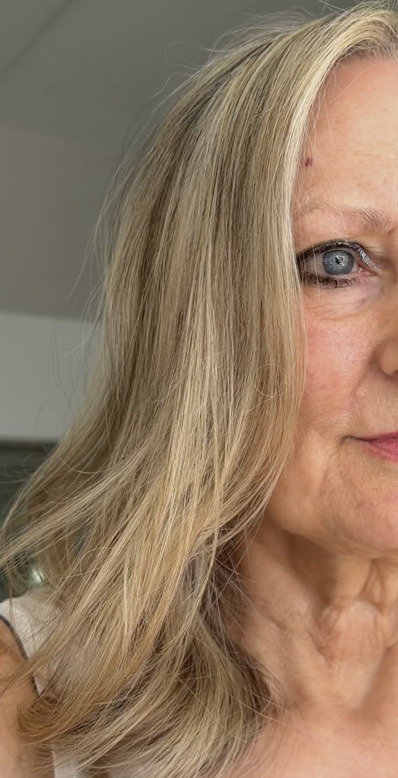 Close-up of a woman with blonde hair and blue eyes looking at the camera, showing part of her face and shoulder.