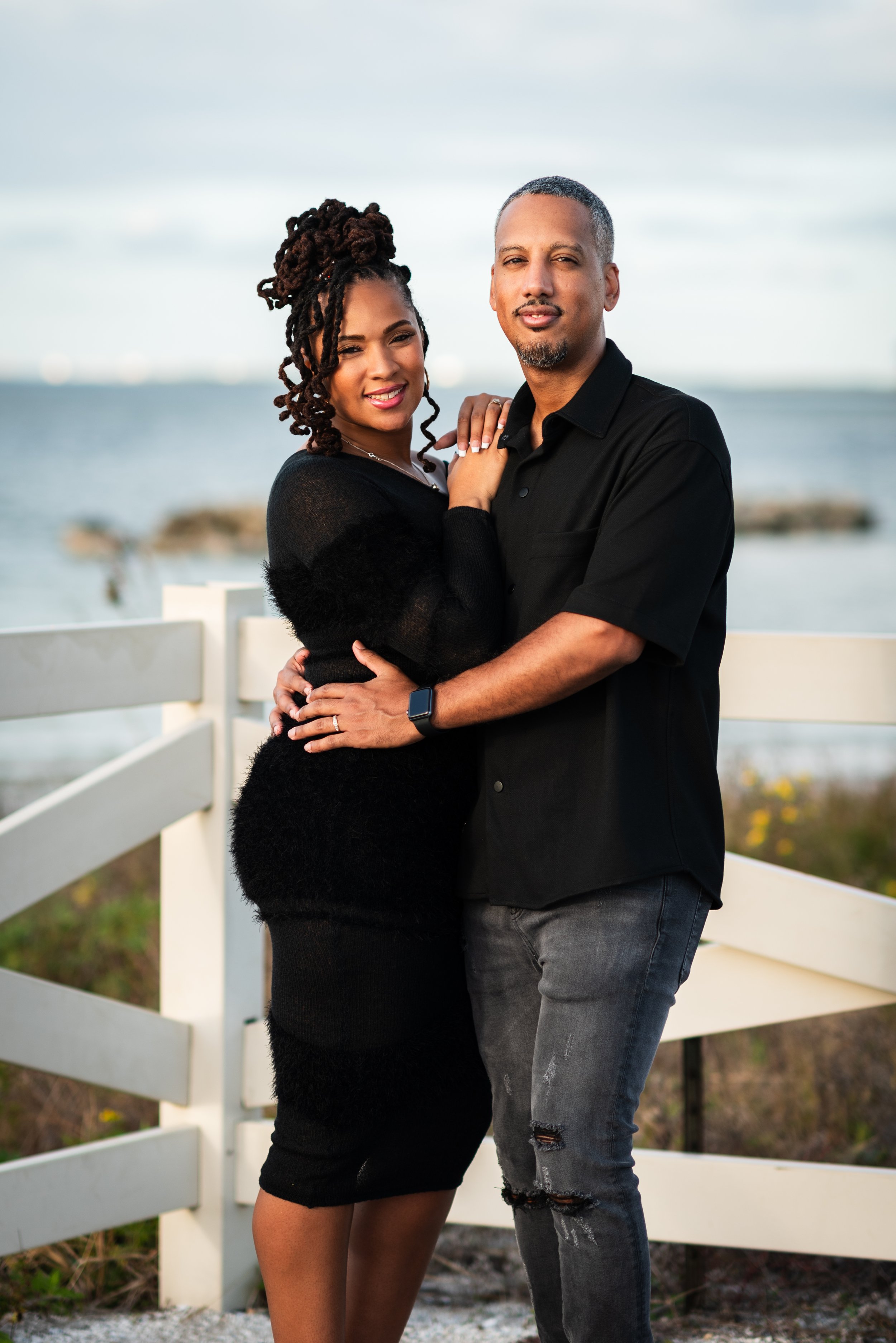 Couple's portrait embracing in front of a white fence at Apollo Beach Nature Preserve, Tampa Bay
