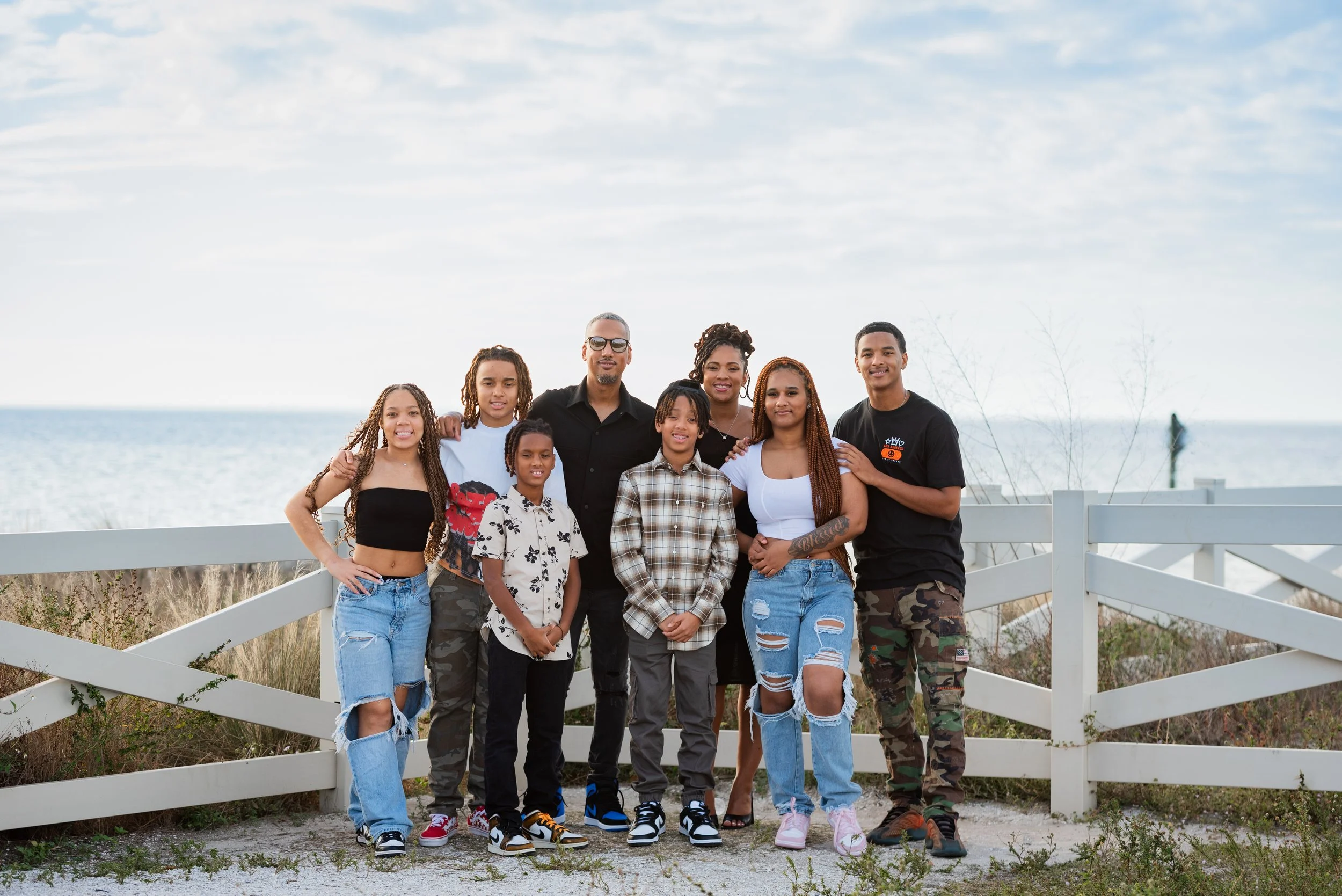 Full extended family group portrait standing in front of a white fence overlooking the water at Apollo Beach Nature Preserve