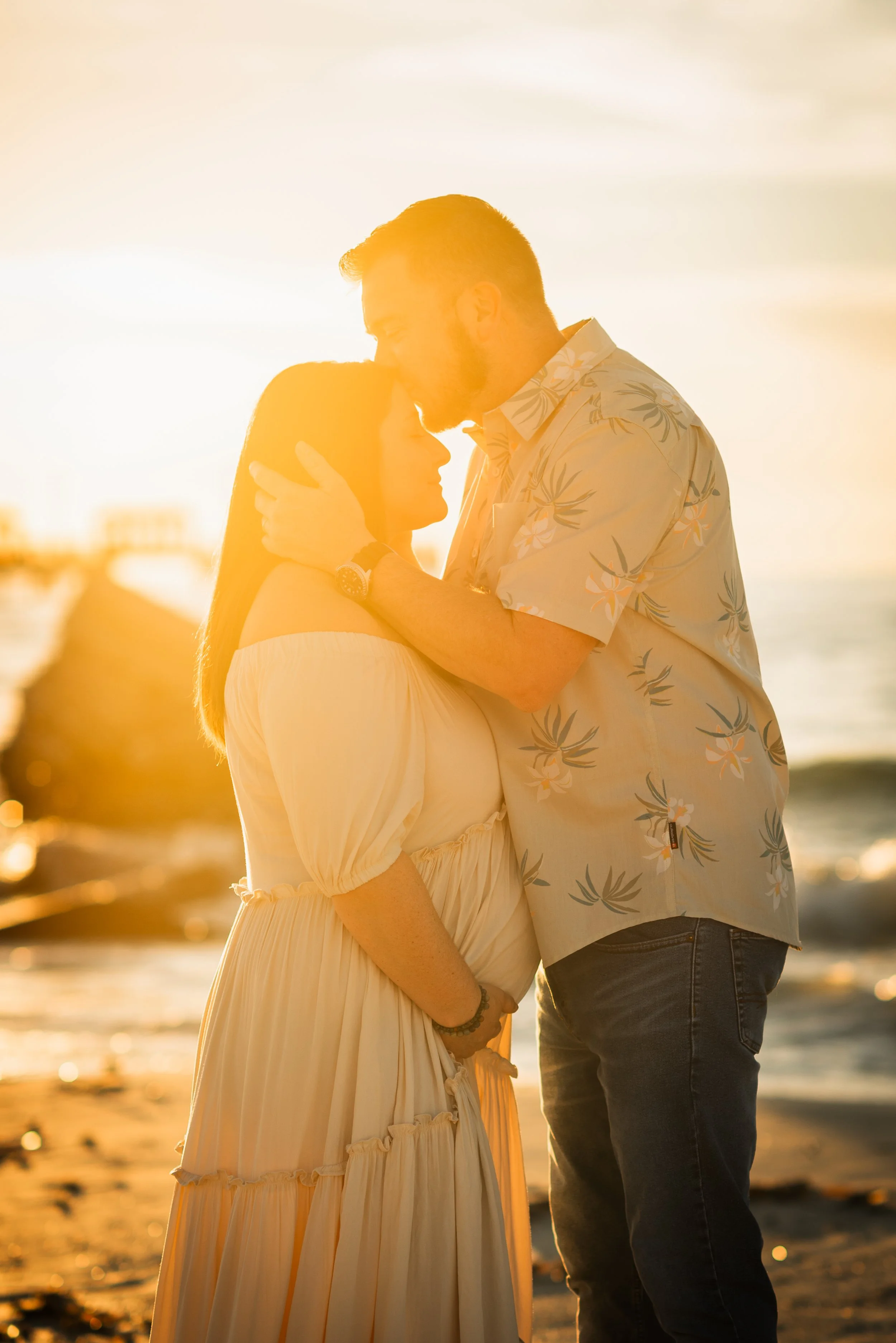 Husband kissing wife's forehead during golden hour maternity session, Fort De Soto