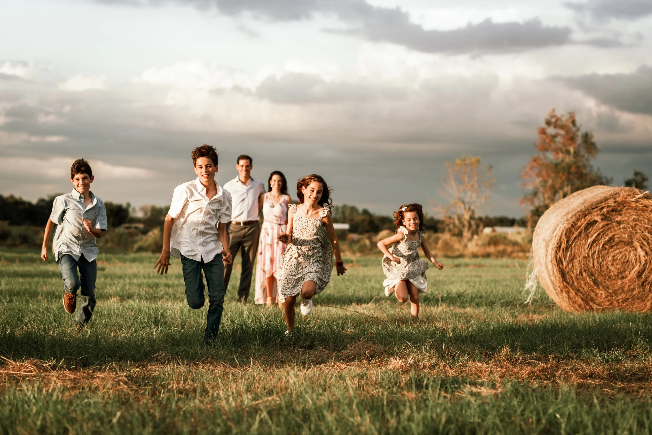 Kids running through a field toward a hay bale at golden hour, Lithia FL family photo session