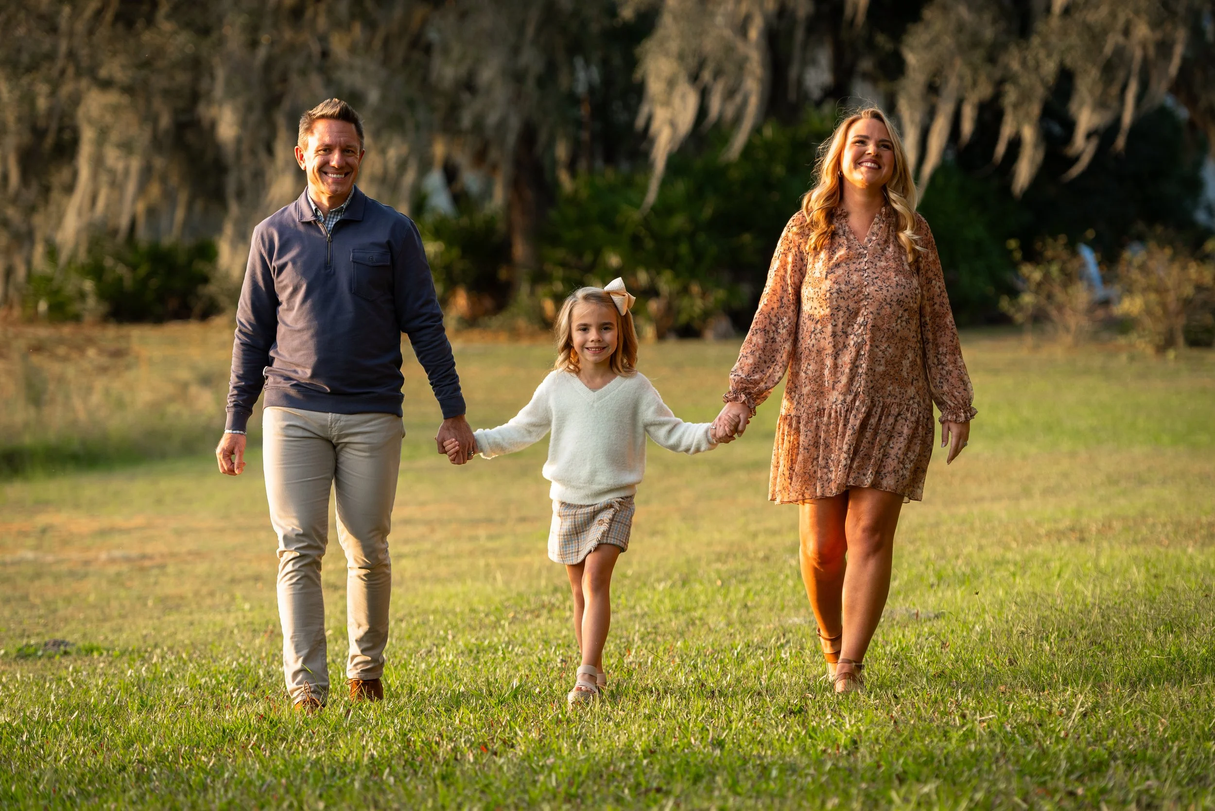 Family of three walking hand in hand across a grassy field