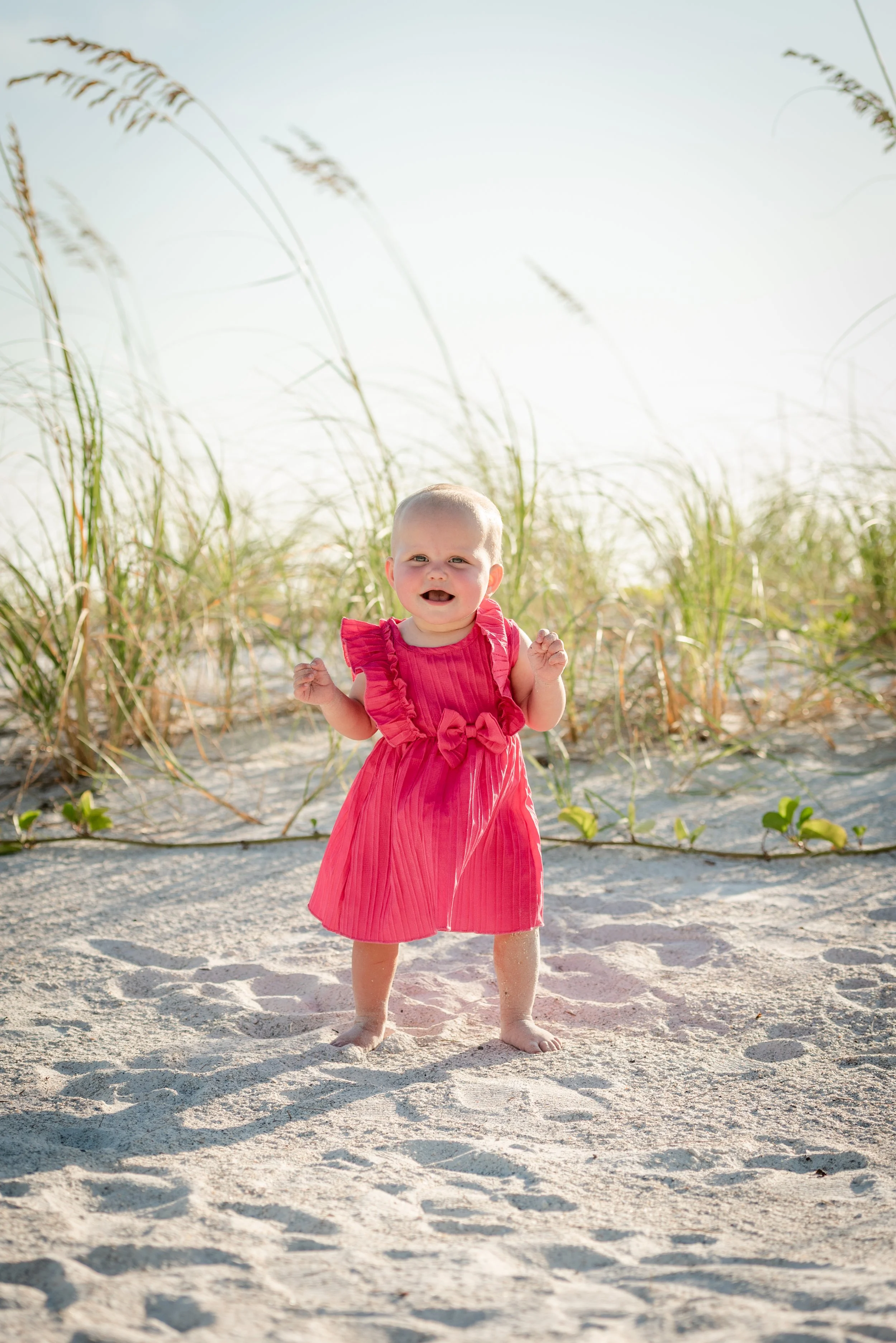 Baby girl in pink dress standing in beach dune grass, Coquina Beach