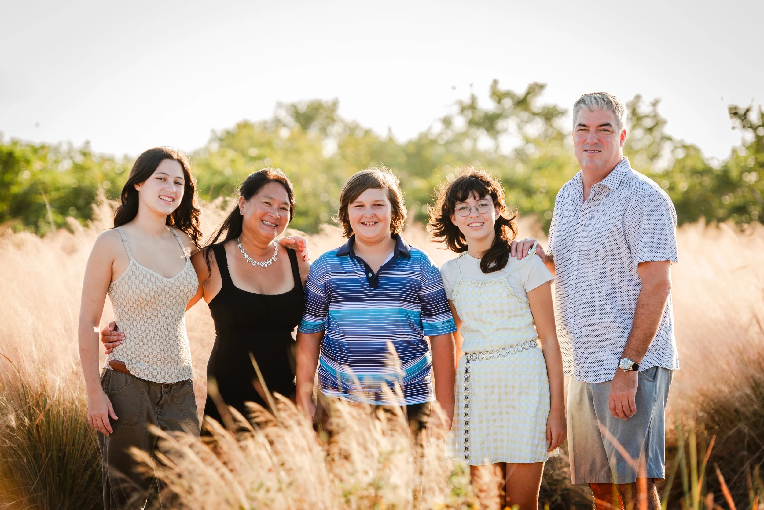 Family of five standing together in tall golden grass at Cypress Point Park