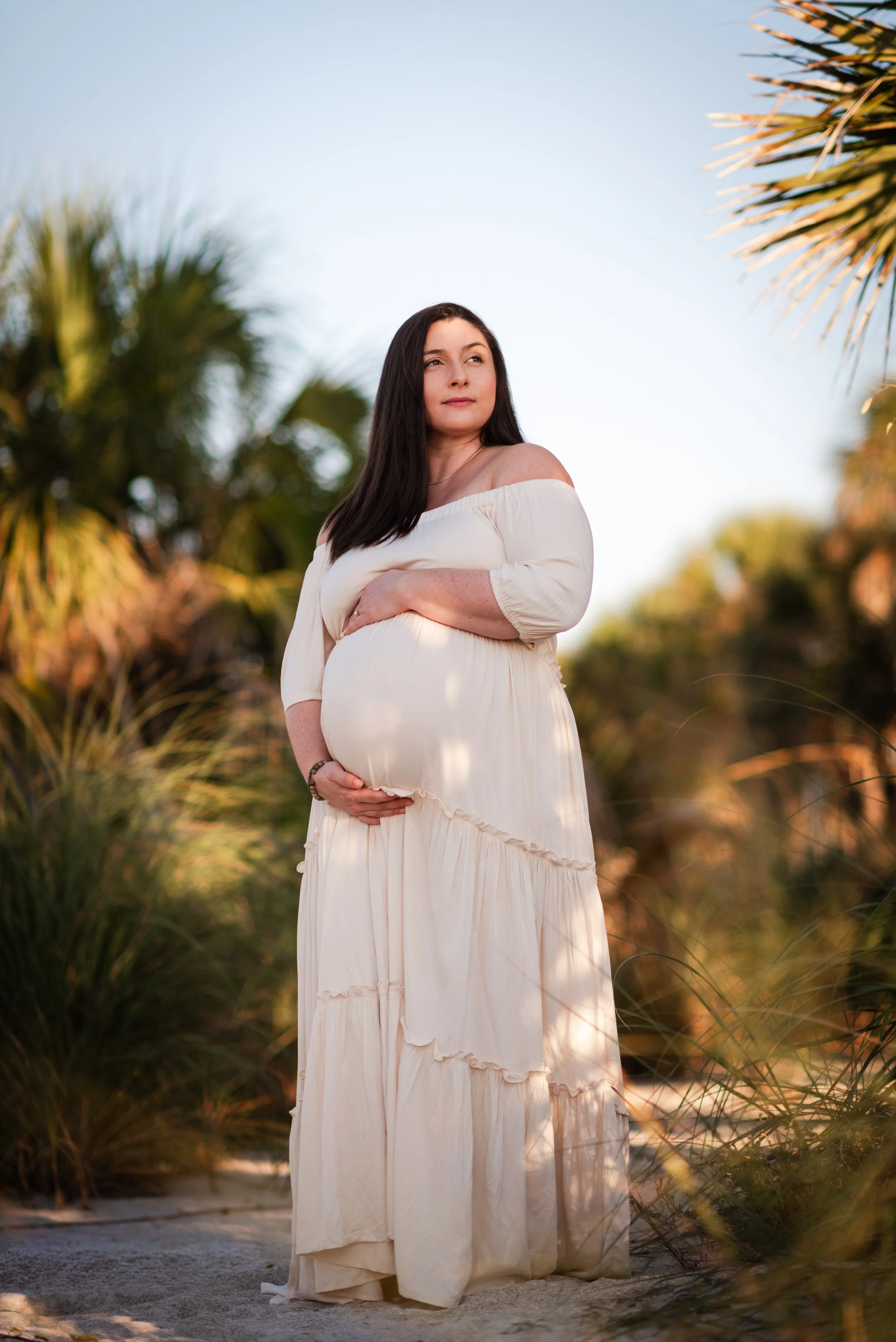 Pregnant woman in flowing white dress among palm trees, Fort De Soto FL