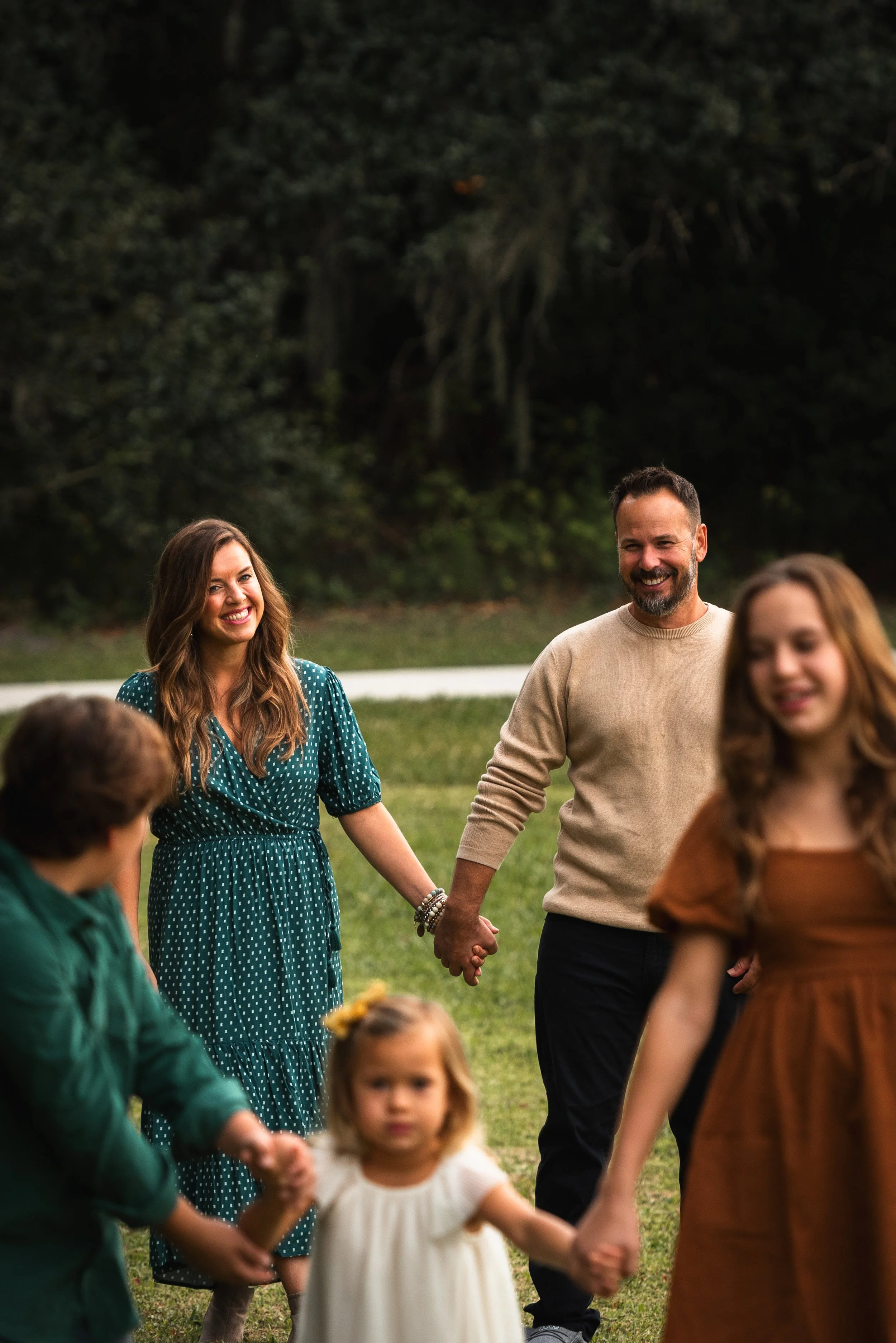Family of five holding hands and laughing in a grassy field