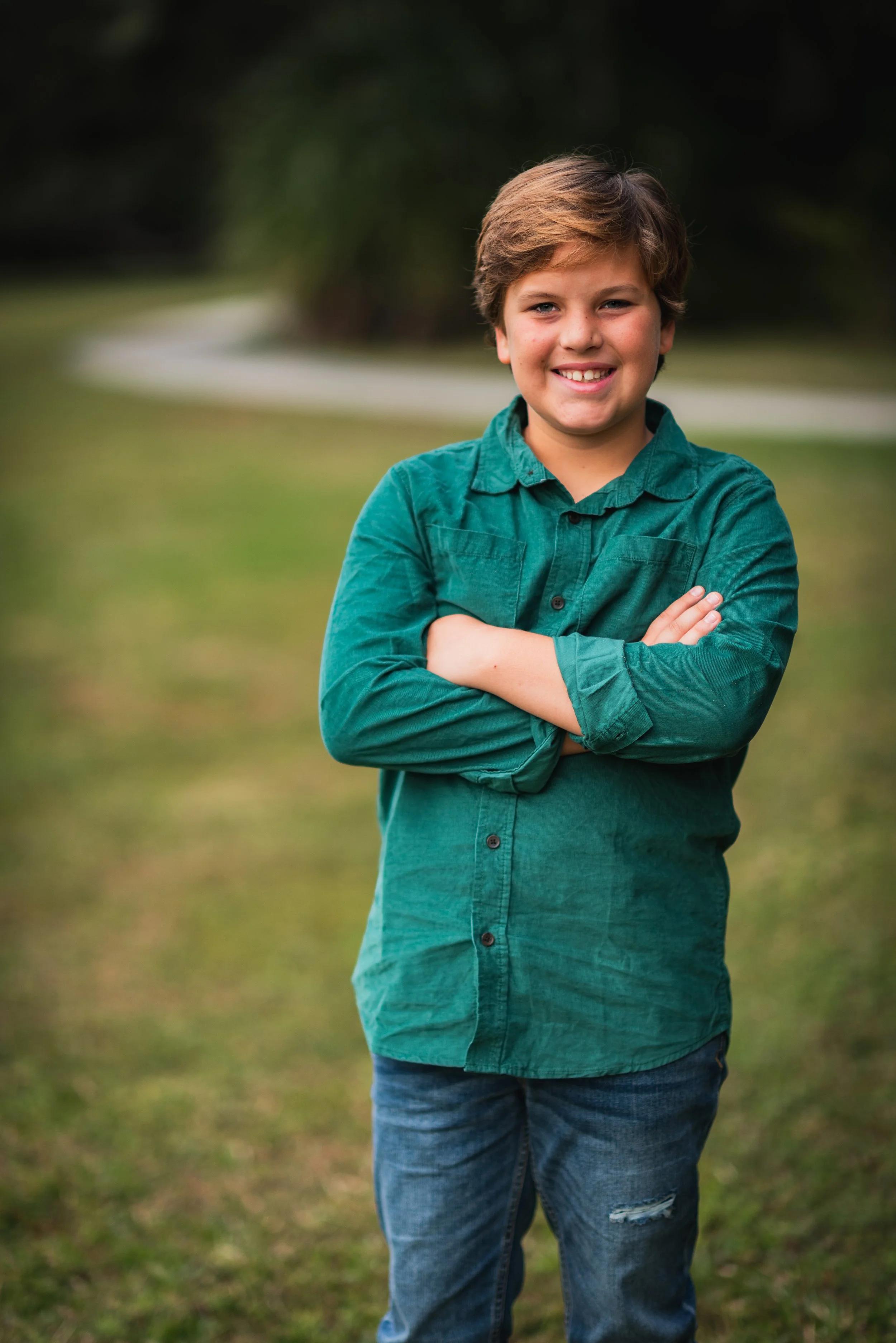 Preteen boy with arms crossed smiling on a garden path