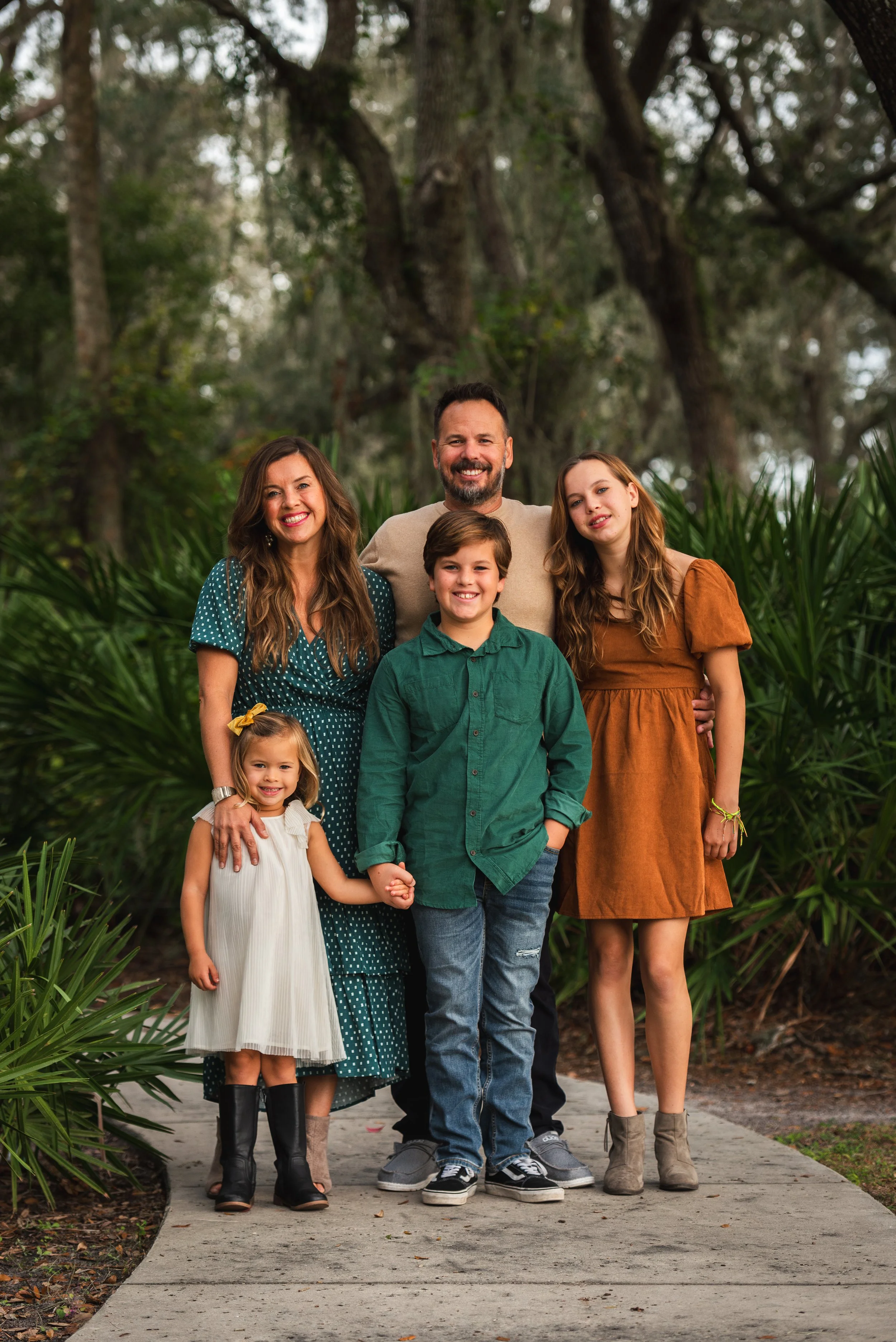 Family of five standing together in a garden path lined with palm trees