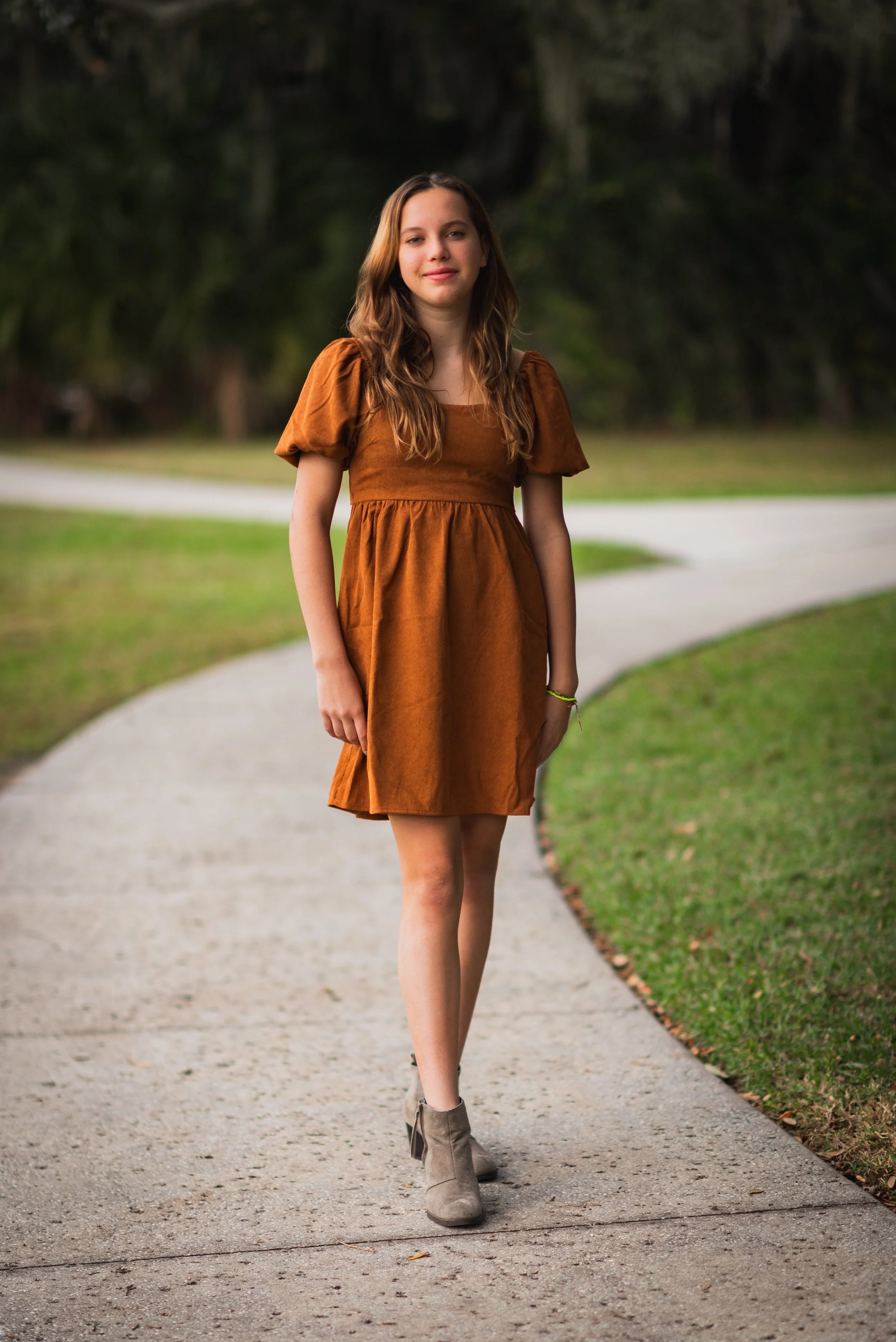 Teenage girl in rust-colored dress walking on a garden path