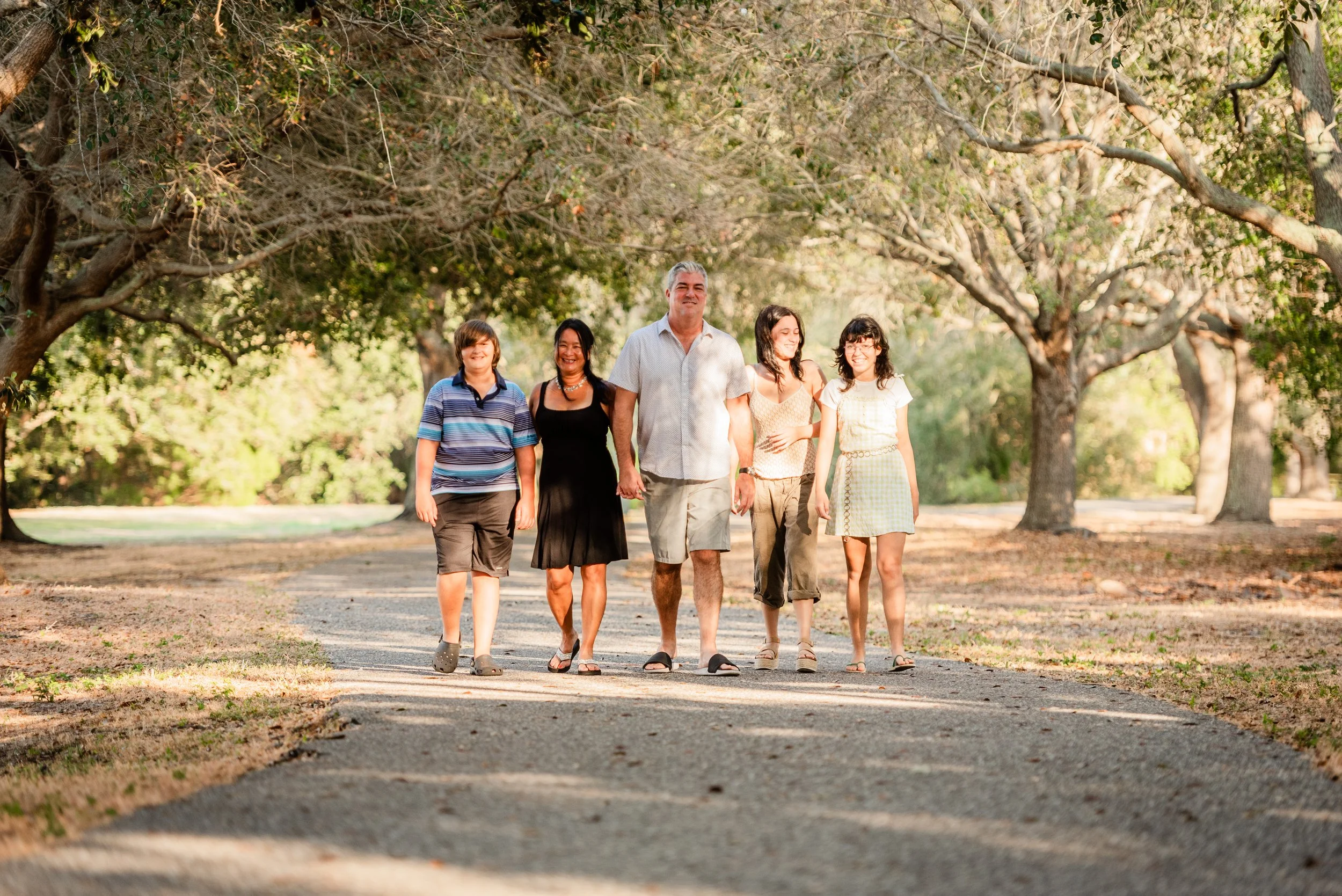 Blended family of five walking together on a tree-lined path at Cypress Point Park, Tampa