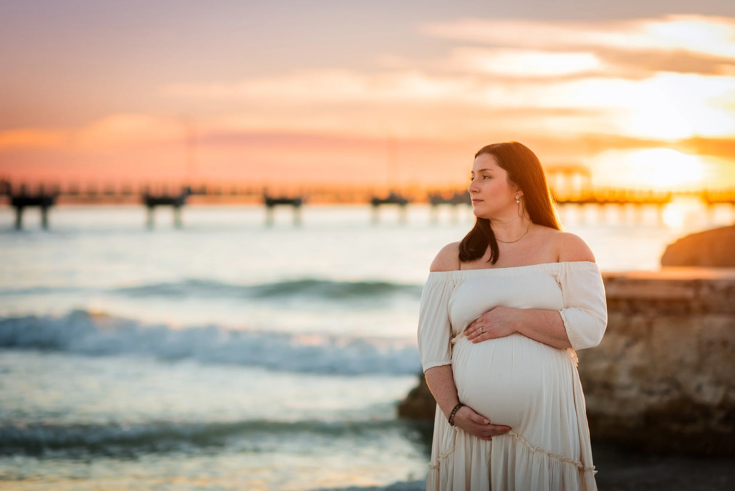 Pregnant woman in white dress standing by the water at sunset, Fort De Soto FL