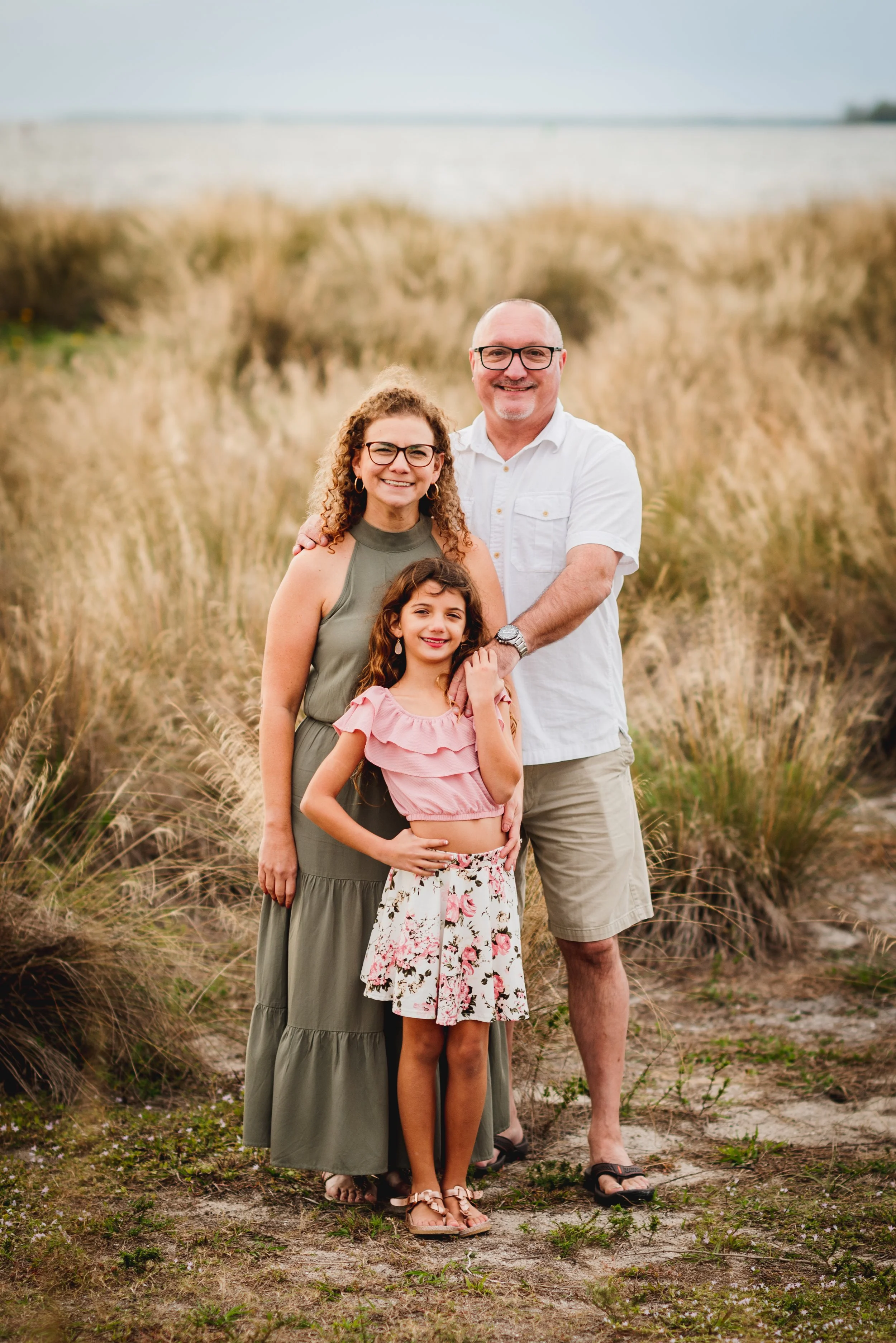 Family portrait of mother, father, and daughter in tall grass at Apollo Beach Nature Preserve