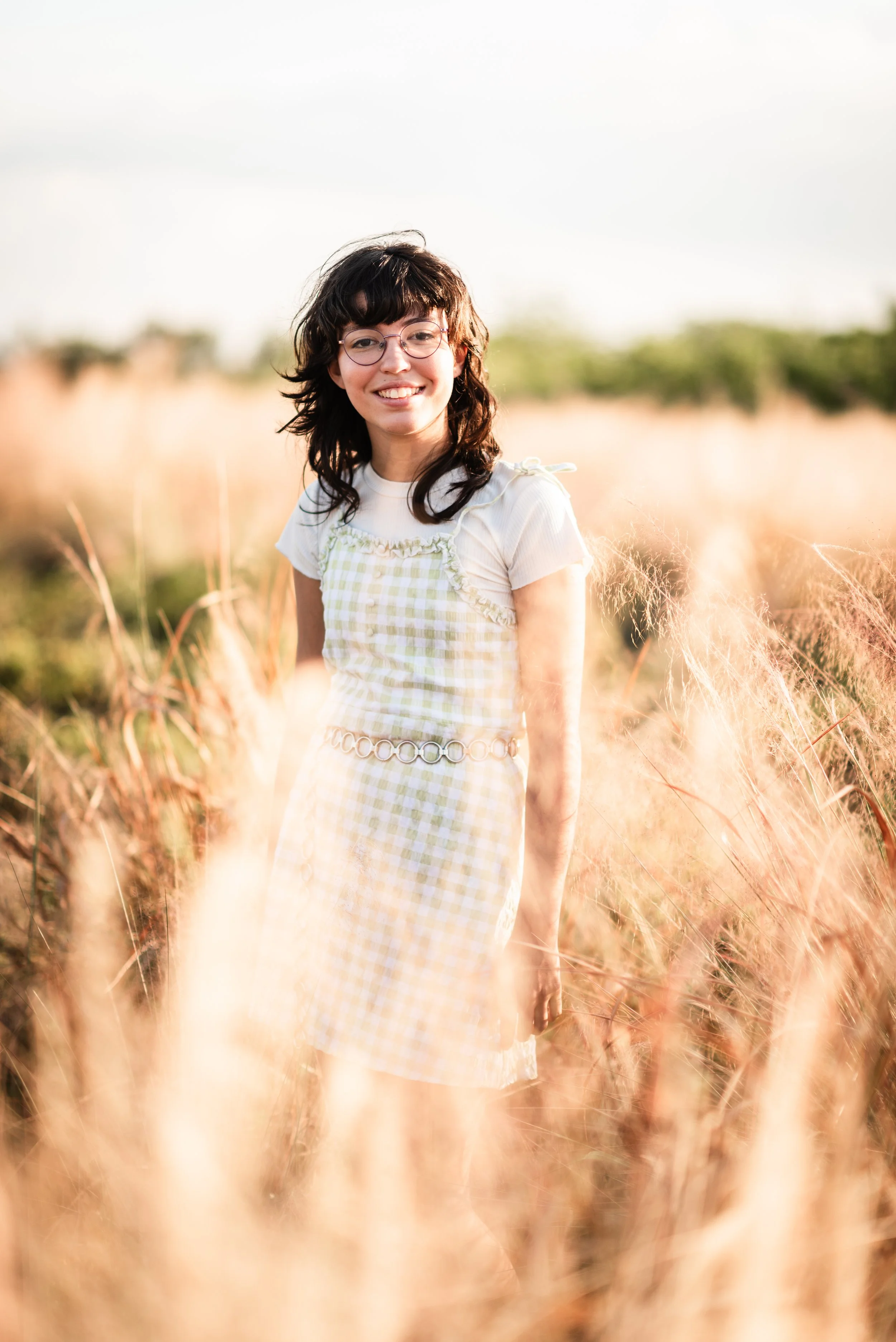 Teenage daughter in a plaid dress standing in a field of tall grass