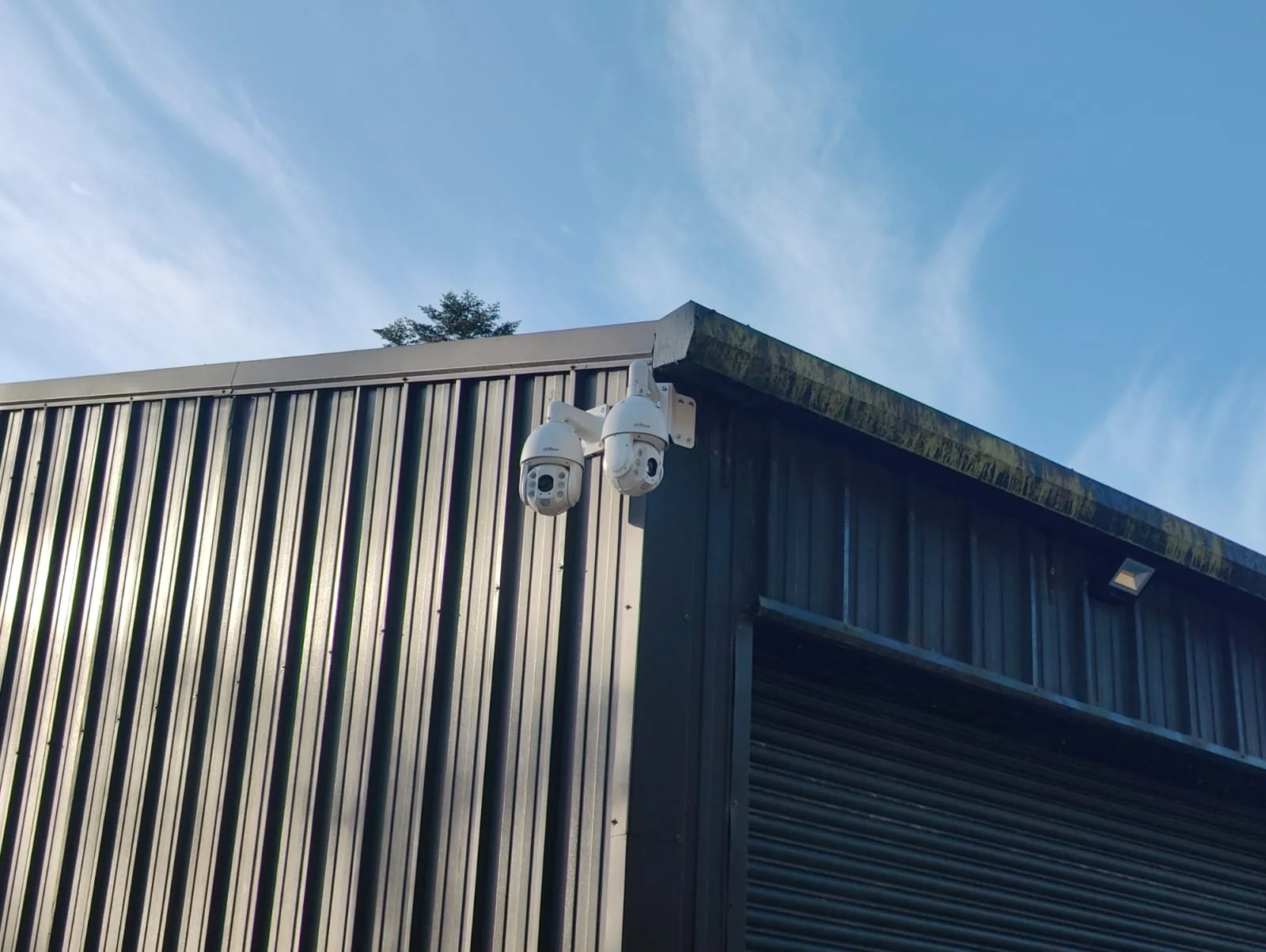Two security cameras mounted on the corner of a building with metal siding, under a clear blue sky.