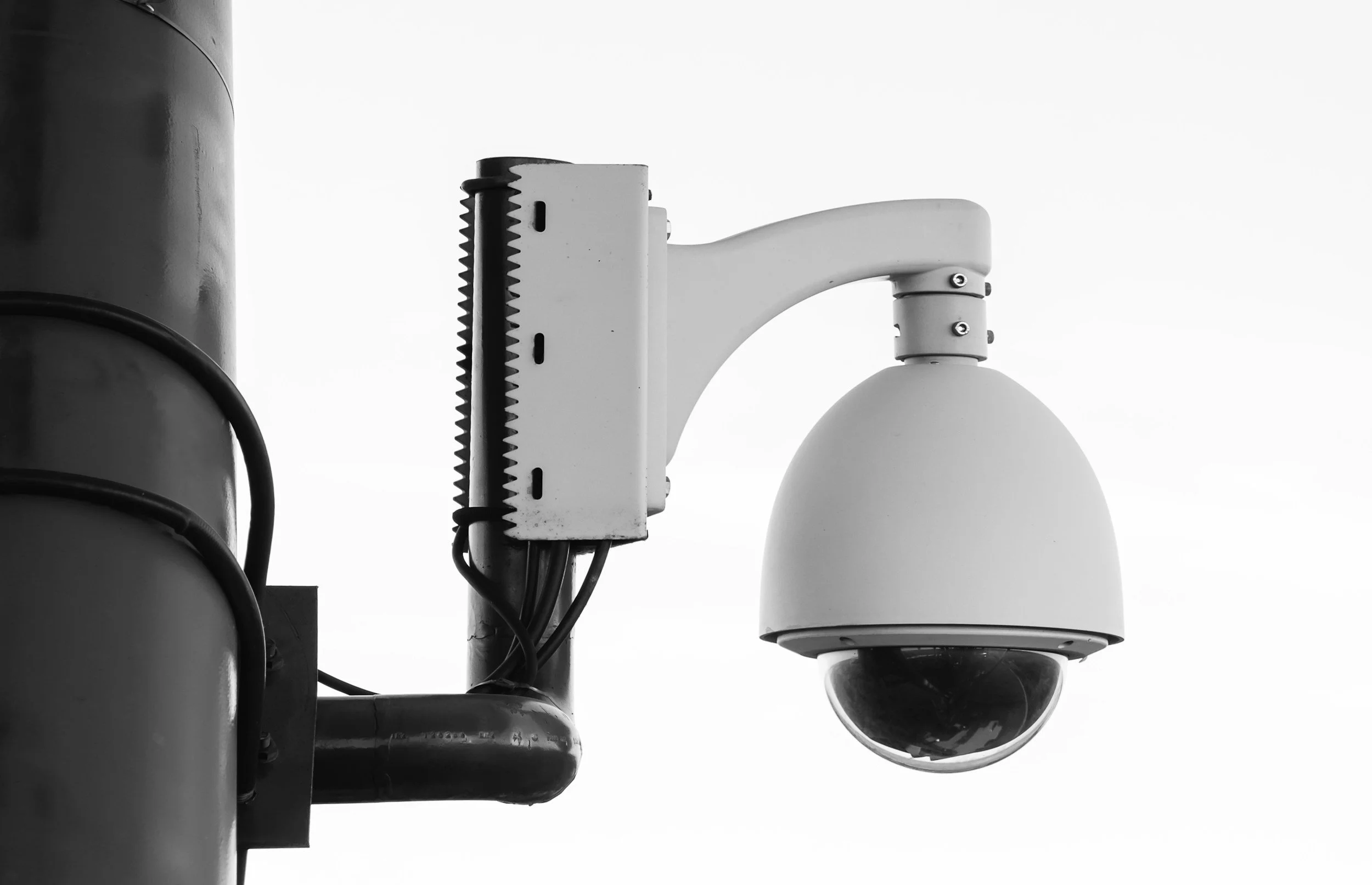 A security camera mounted on a pole against a white sky.