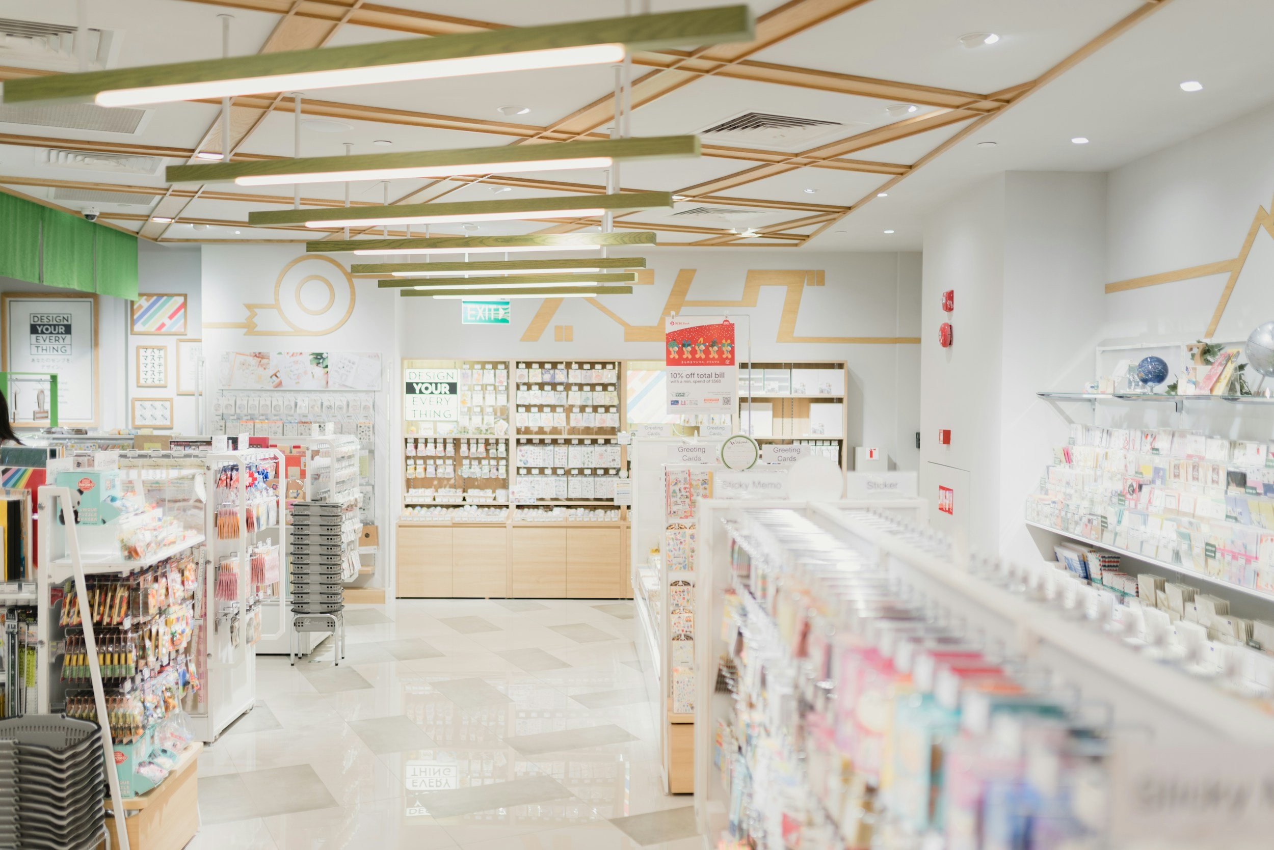 Interior of a stationery store with shelves stocked with various paper products, notebooks, and greeting cards, brightly lit with a modern design.