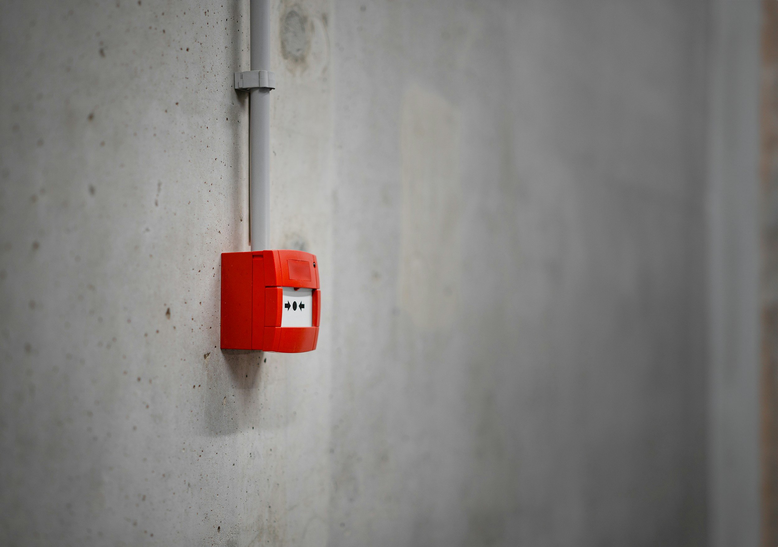 Close-up of a red fire alarm device mounted on a concrete wall.