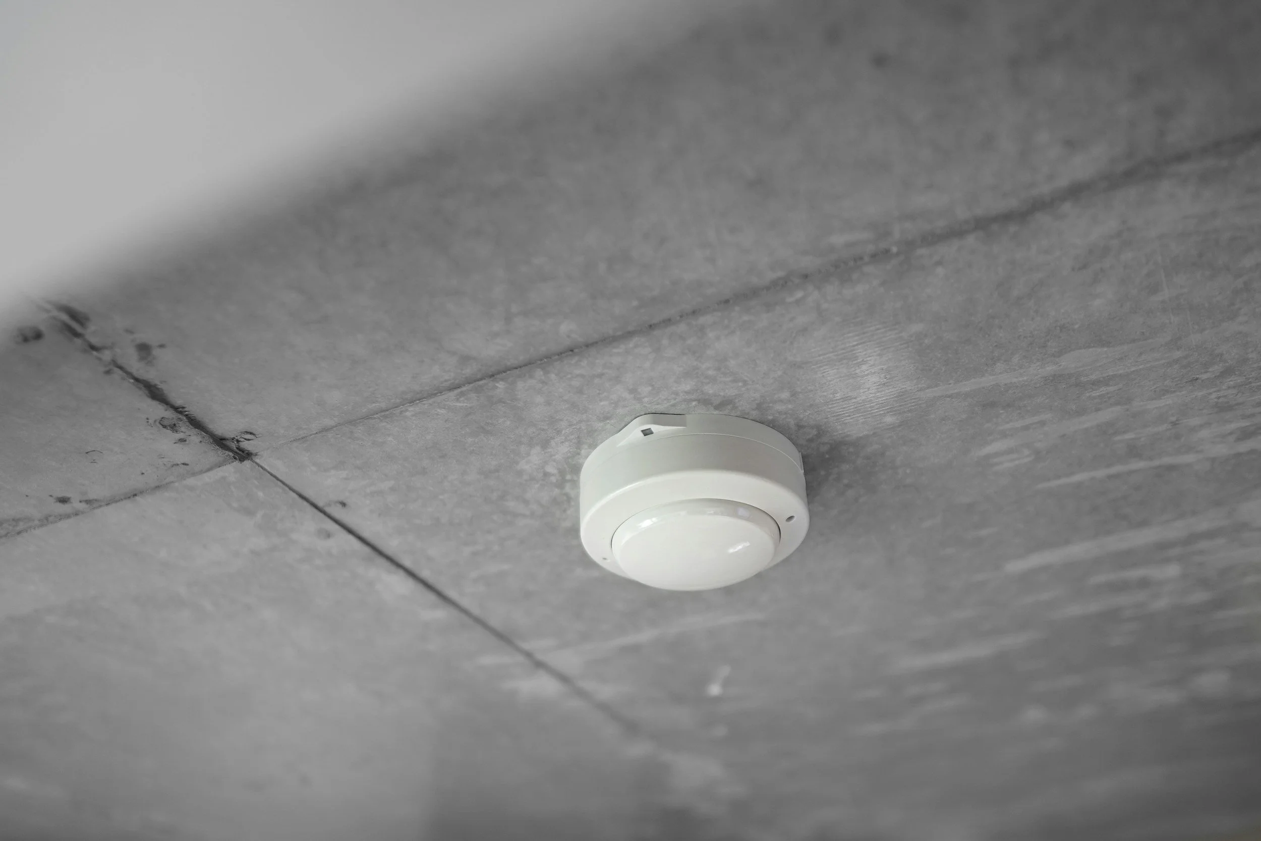 White smoke detector mounted on a gray concrete ceiling.