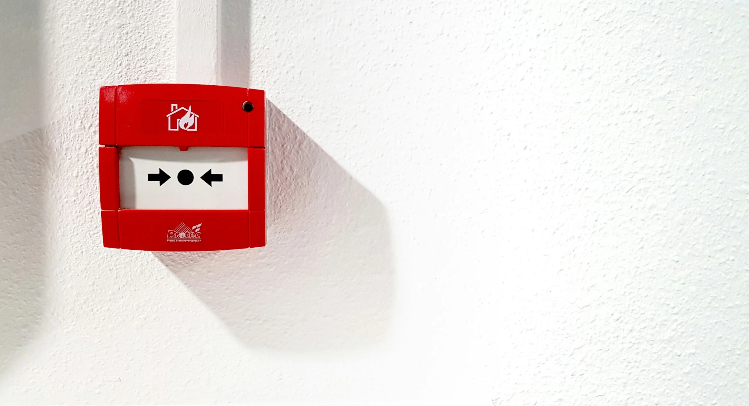 Red fire alarm pull station mounted on a white textured wall.