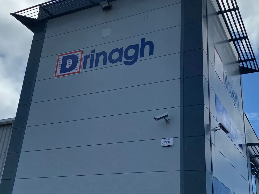 Exterior of a commercial building with a sign reading "Drinagh" and security cameras mounted on the wall.
