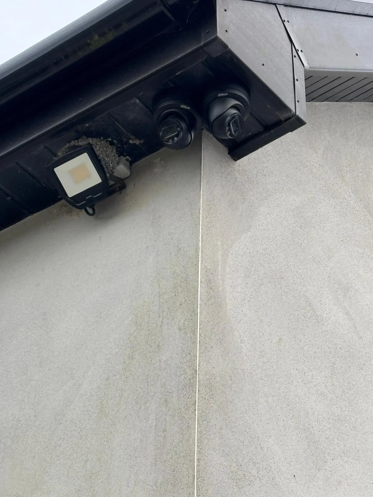 Close-up photo of an exterior wall with two security cameras mounted on black fixtures under a building's overhang.