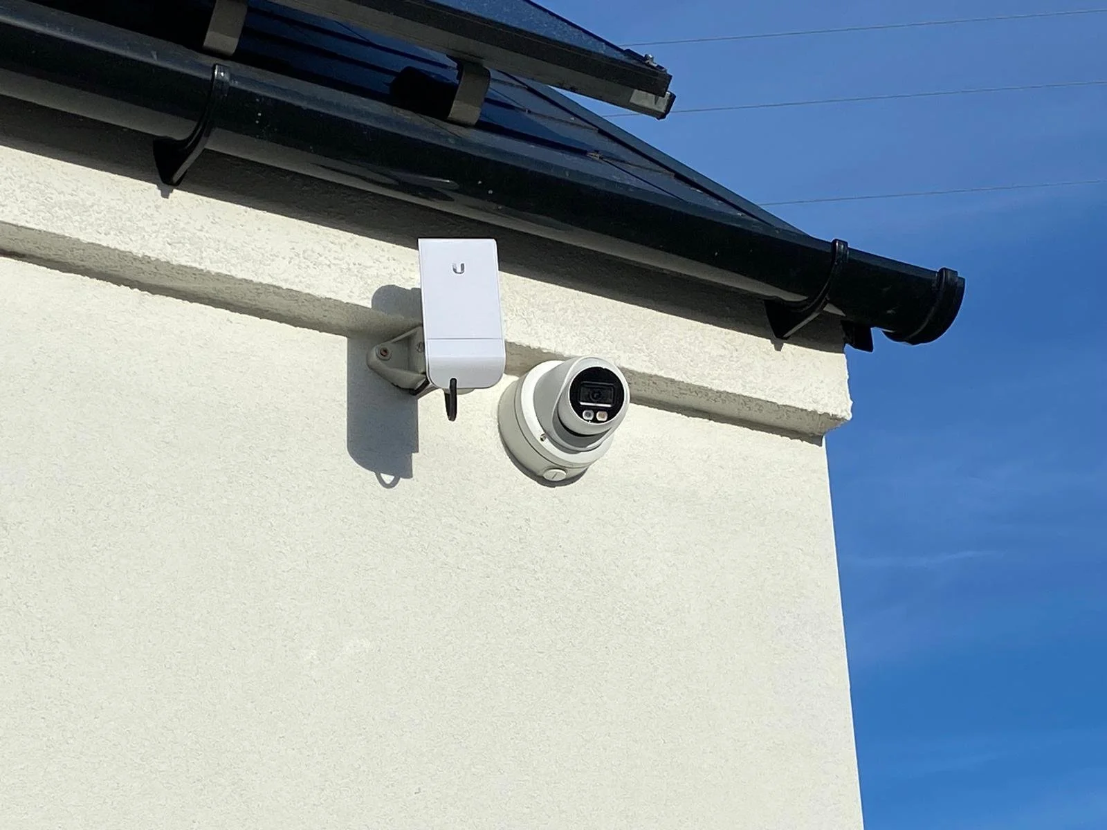Security camera and Wi-Fi router installed on the exterior white wall of a building under a blue sky.
