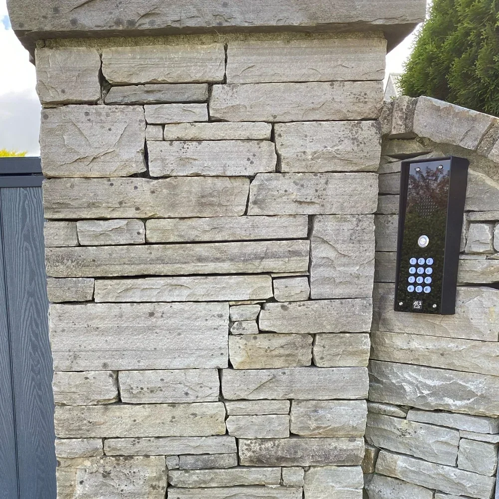A stone wall with a black intercom system attached to it, located outdoors.