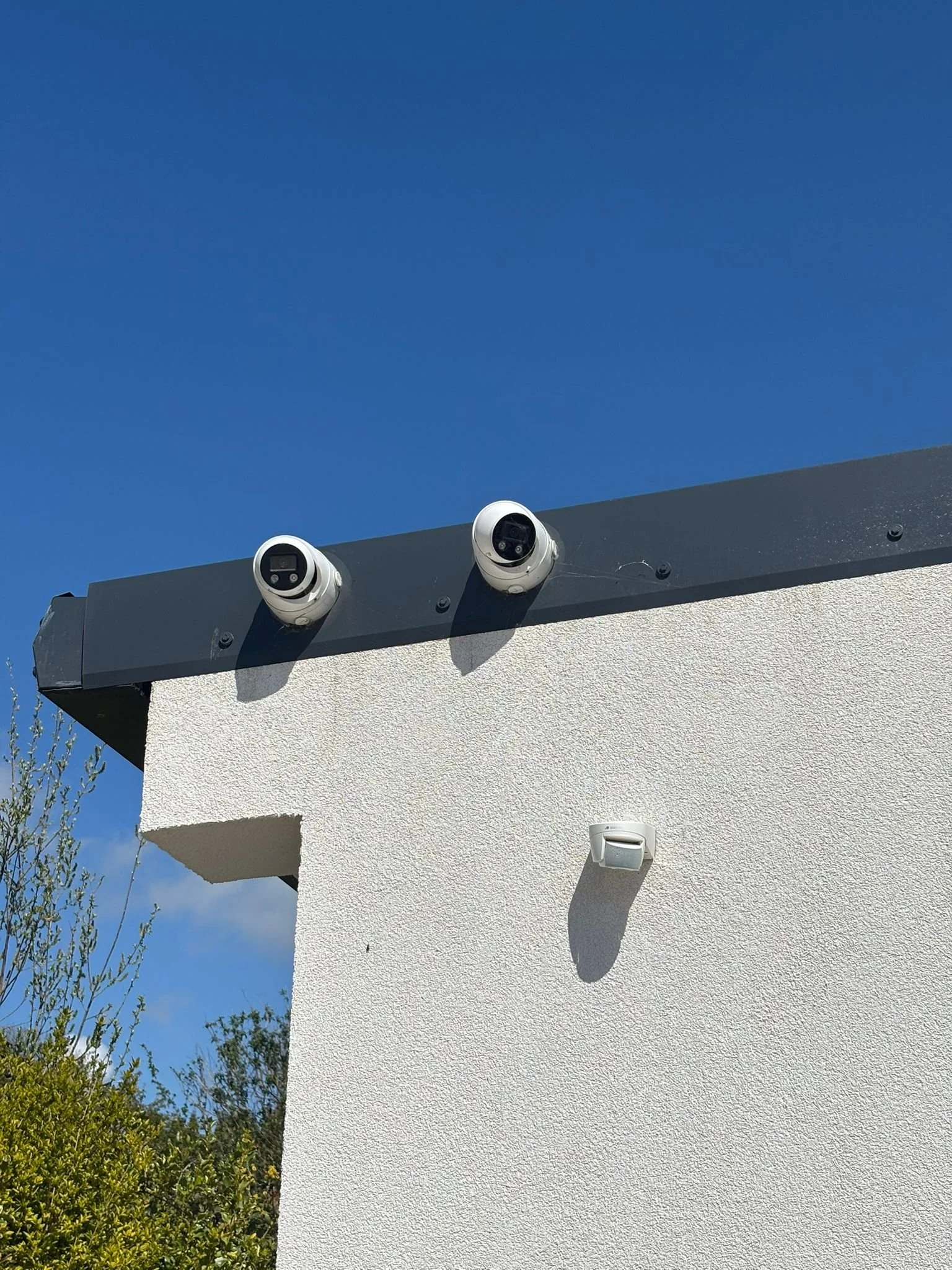 Two security cameras mounted on the corner of a building with a white exterior, under a clear blue sky.