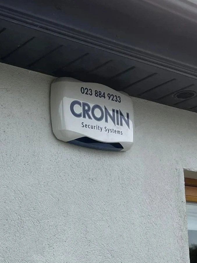 Security alarm system box on a white wall with the company's phone number and name 'CRONIN Security Systems'.