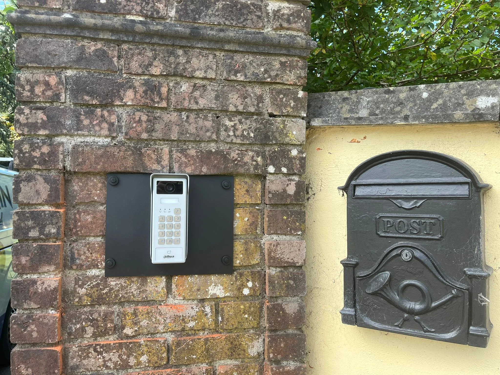 A brick wall with a modern intercom or doorbell system and a yellow wall with a metal mailbox labeled 'POST.'