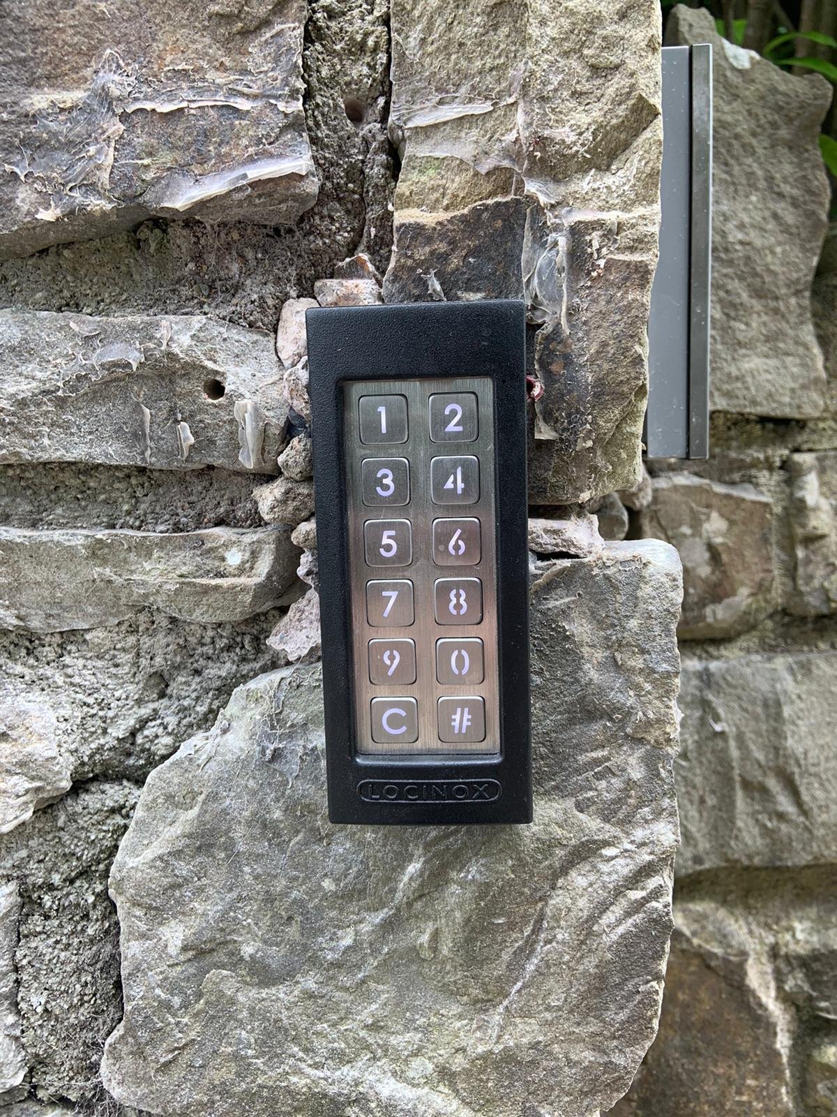 A black and silver numeric keypad lock mounted on a stone wall, with numbers 1 through 9, 0, a C button, and a # button.