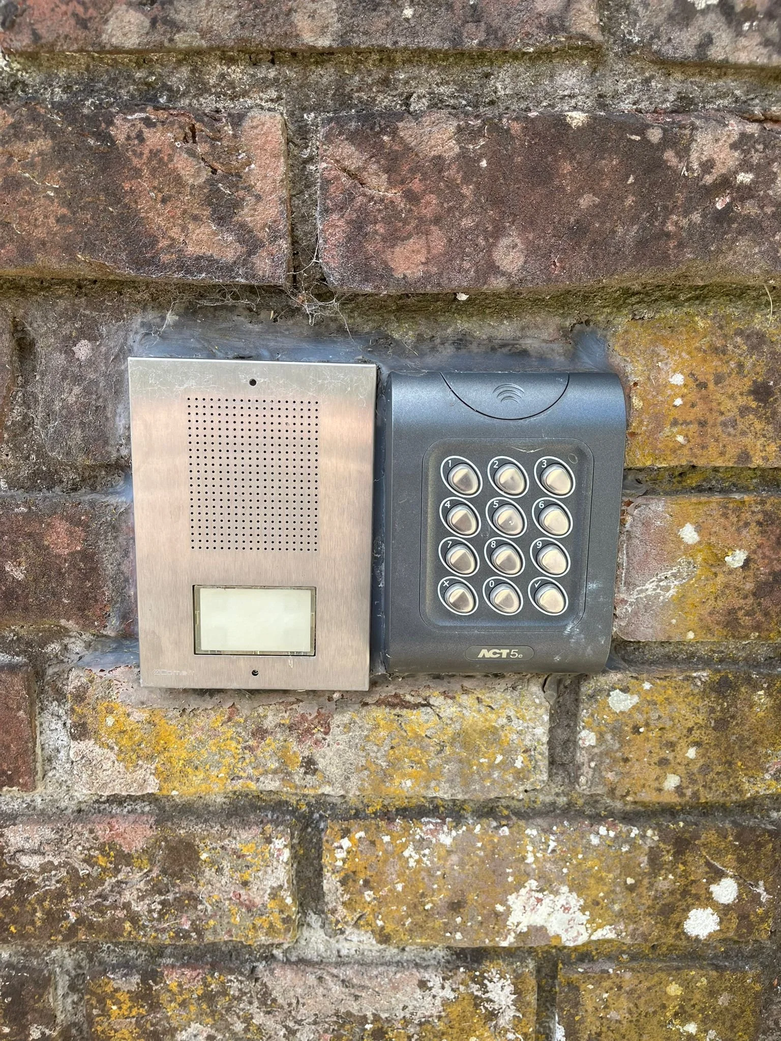 An intercom system with a keypad and a separate speaker/microphone unit mounted on a brick wall.