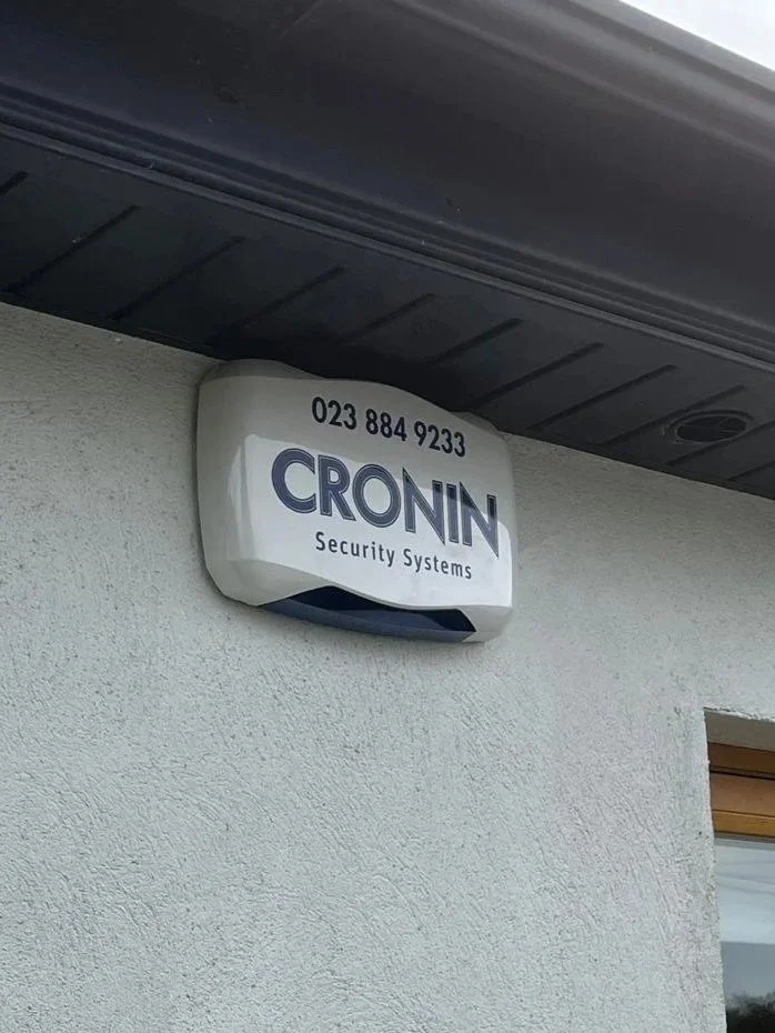 Security alarm sign on a wall displaying the company name 'CRONIN' and a phone number.