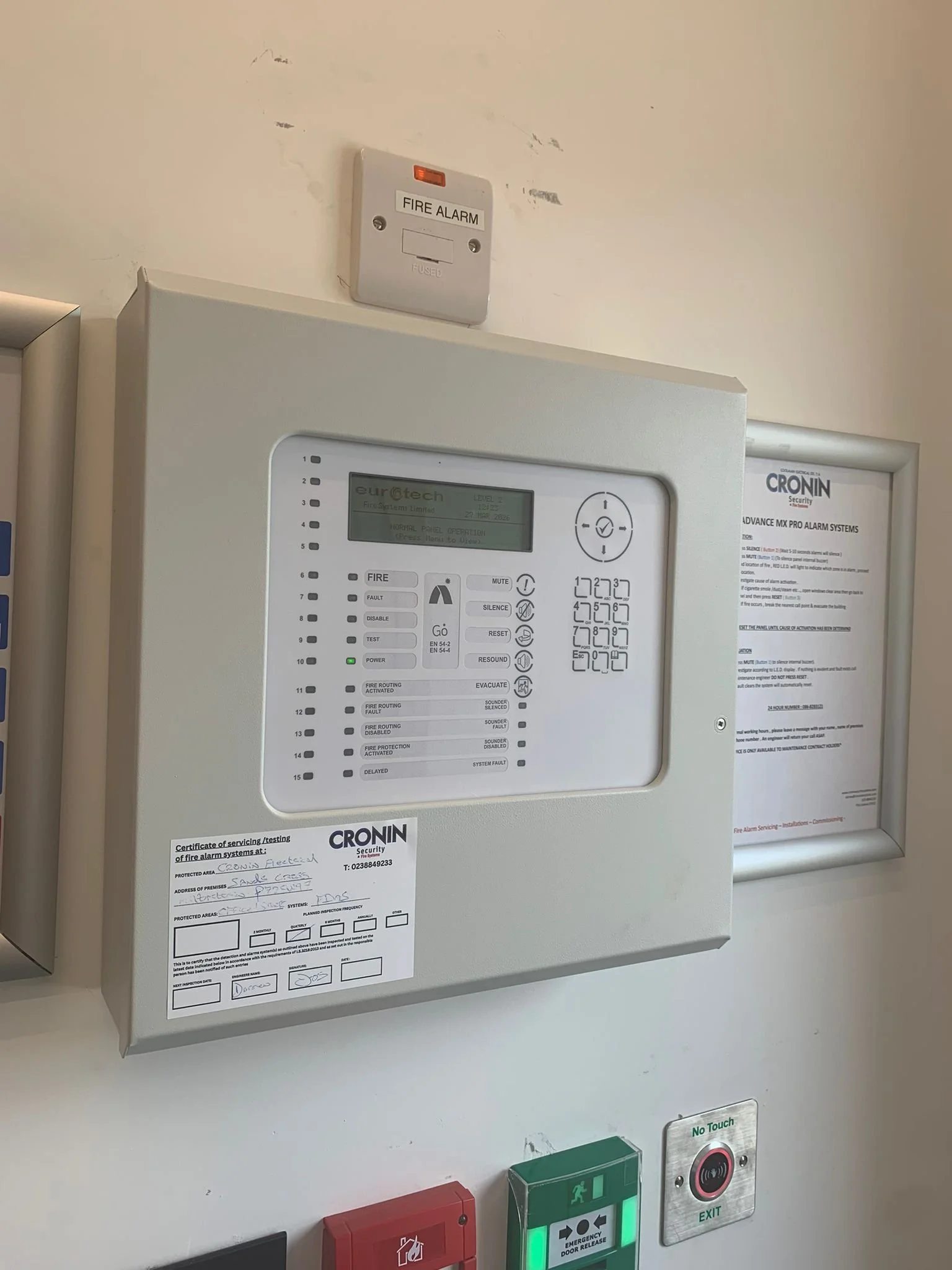 Fire alarm system, fire alarm control panel, emergency exit sign, fire safety equipment, and a no touch emergency button display on a wall.
