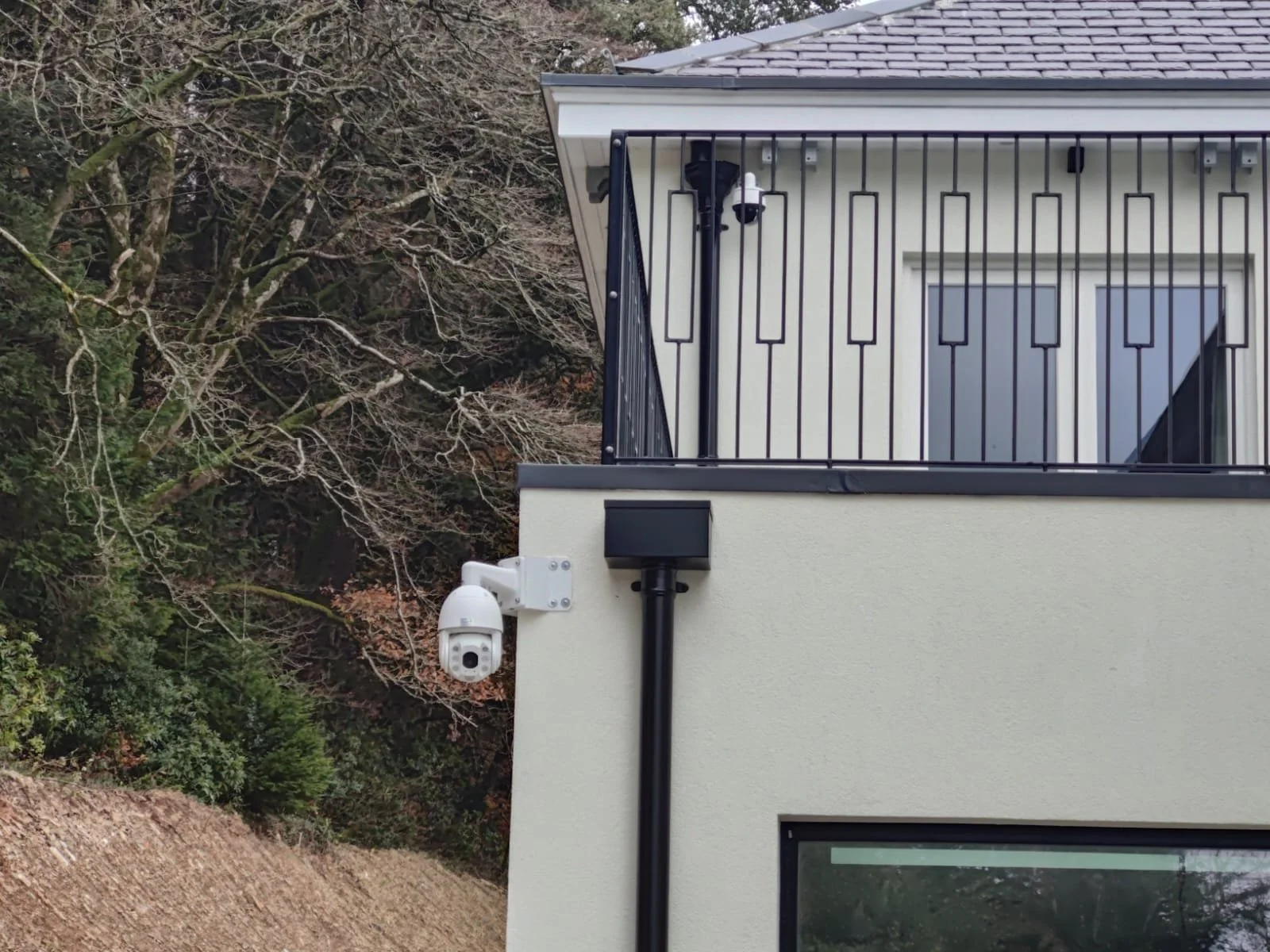 Close-up of a modern building's corner with security cameras and a surveillance box mounted on the wall, and a balcony with black railing.