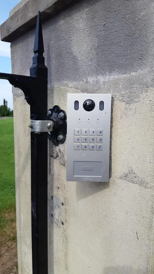 A silver intercom device mounted on a red brick wall outside a building.