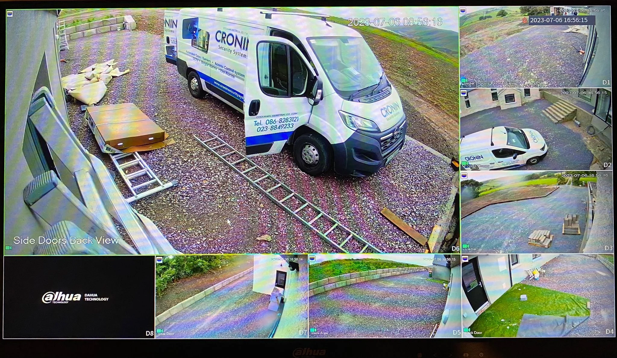 Surveillance camera footage featuring a white security van and a silver vehicle parked outside near a structure. The van has blue and white branding for CROWN Security Systems. Multiple camera angles show the surrounding area, including steps, pallets, and a grassy patch.