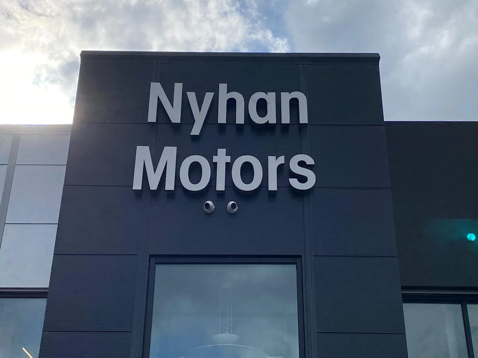 Building with large sign reading 'Nyhan Motors' against a cloudy sky.