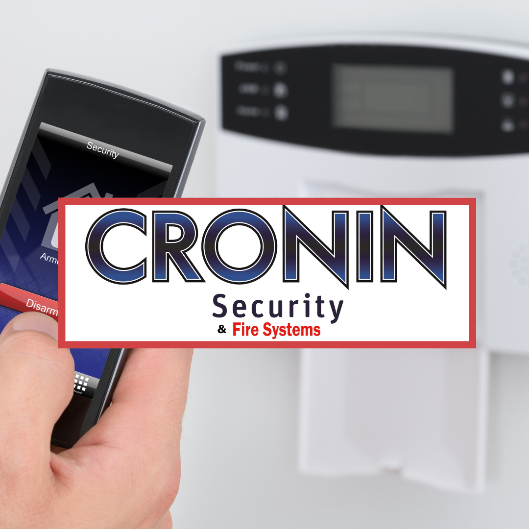 Person using a remote control to arm a security system in front of a control panel with the logo 'CRONIN Security & Fire Systems' overlayed.