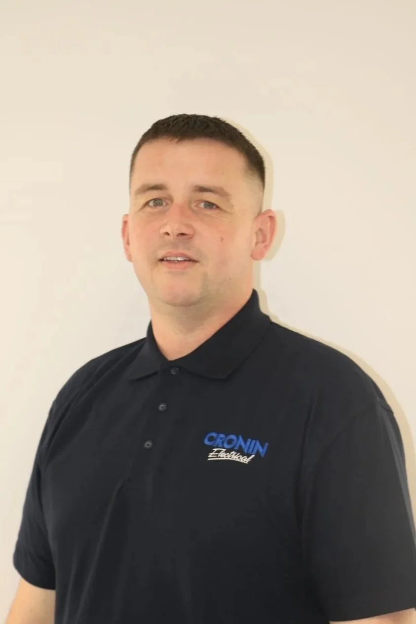 A man with short dark hair wearing a black polo shirt with 'CRONIN Electrical' logo posed against a plain white wall