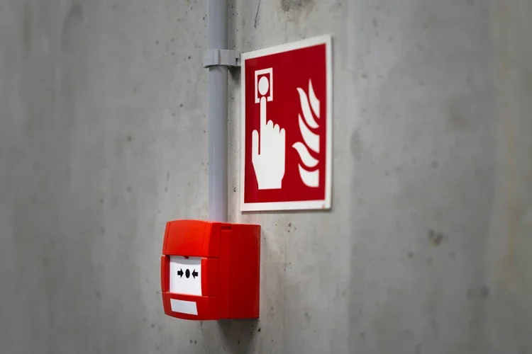 Red fire alarm pull station beneath a fire safety sign on a concrete wall.