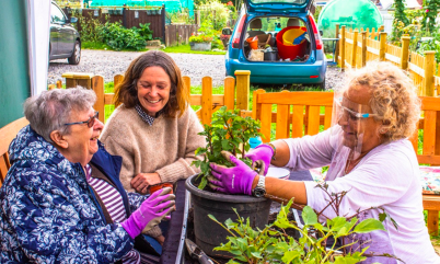 photo of three people potting plants in their garden while sat on a bench