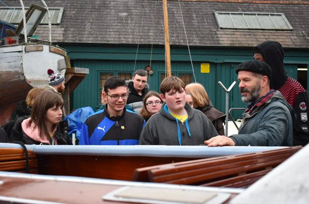 group of people stood outside of an industrial building  looking at a boat